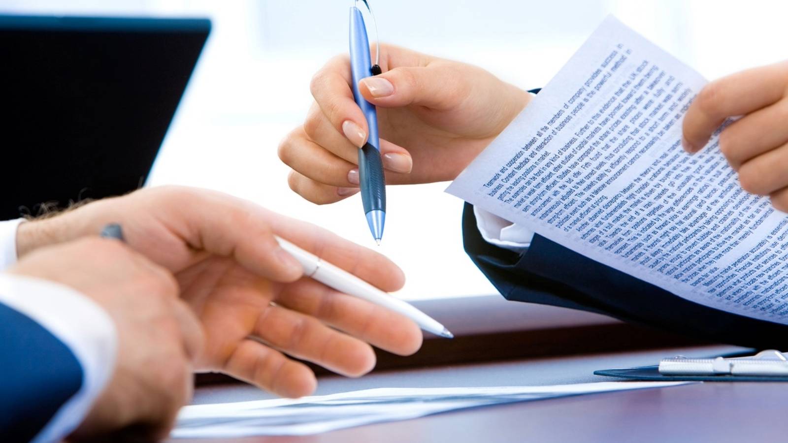 closeup of two individuals hands in office setting holding paperwork and pens in mid discussion