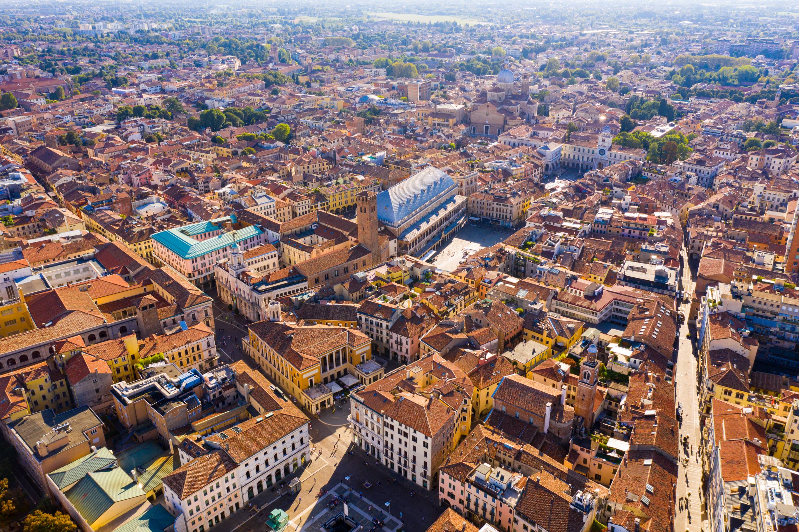 Aerial view of densely populated Padova, Italy, showcasing its vibrant plazas, interconnected roads, and abundant greenery, with notable landmarks visible in the landscape.