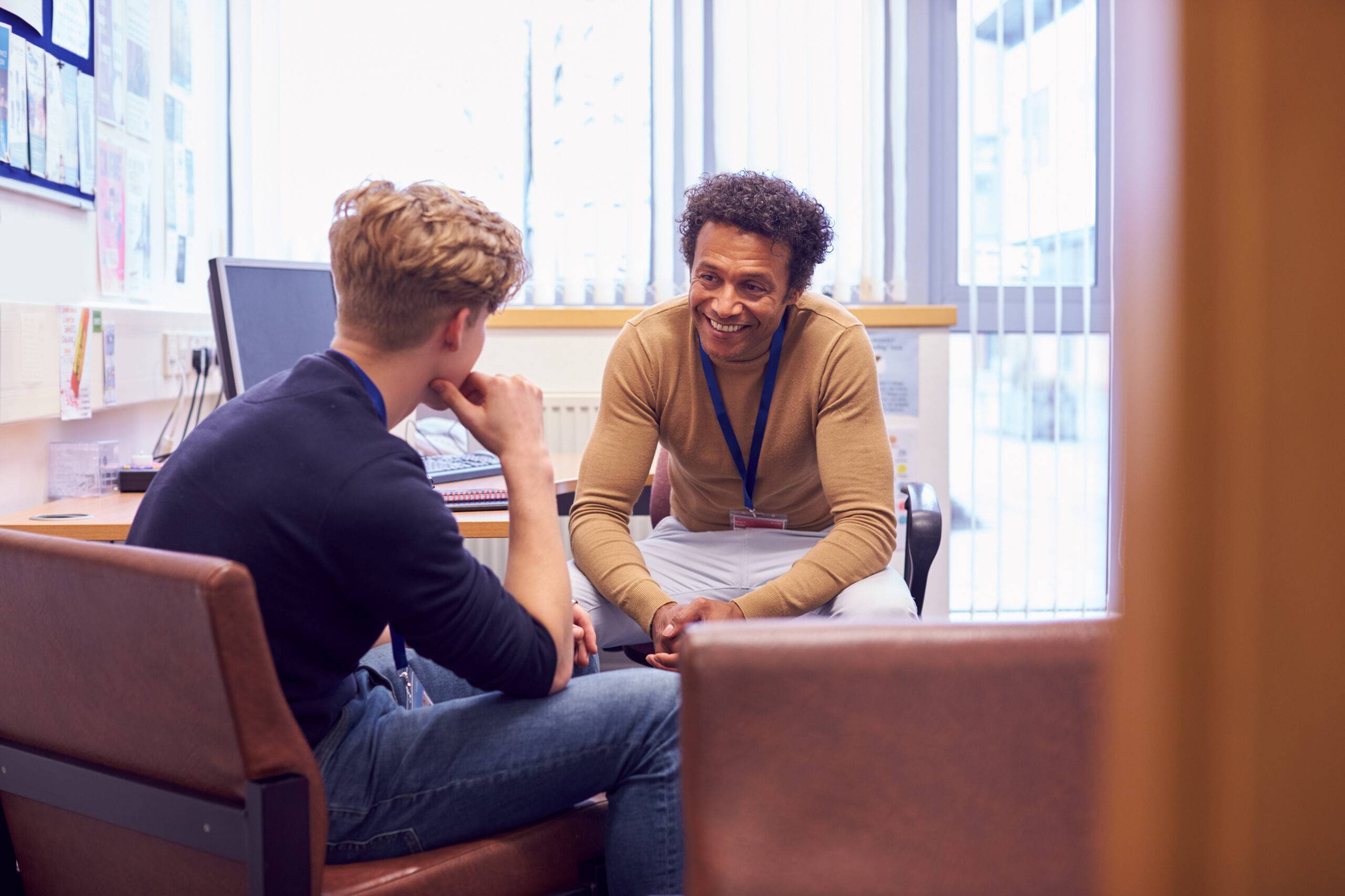 Two men in an office sitting at a desk having a conversation.