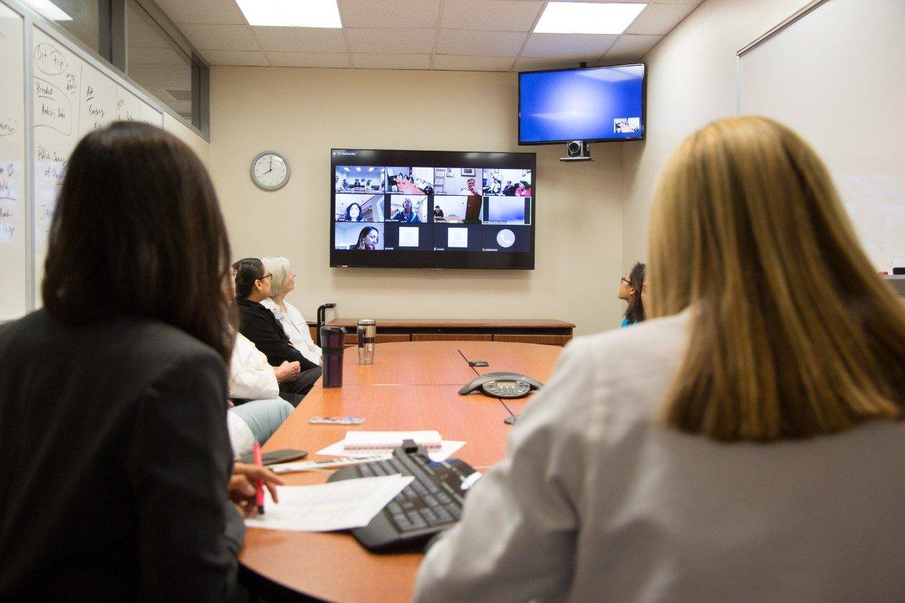 A large group of researchers sitting at a conference table during a virtual meeting.