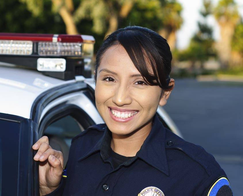 A female police officer smiling as she leans against the cop car.