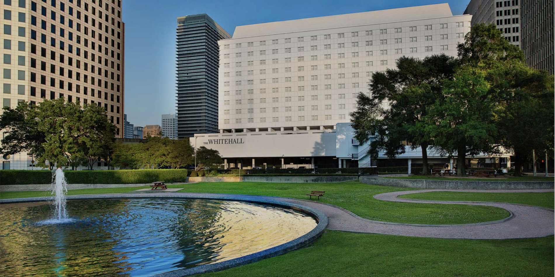 A large water fountain in a park with a large building in the background.