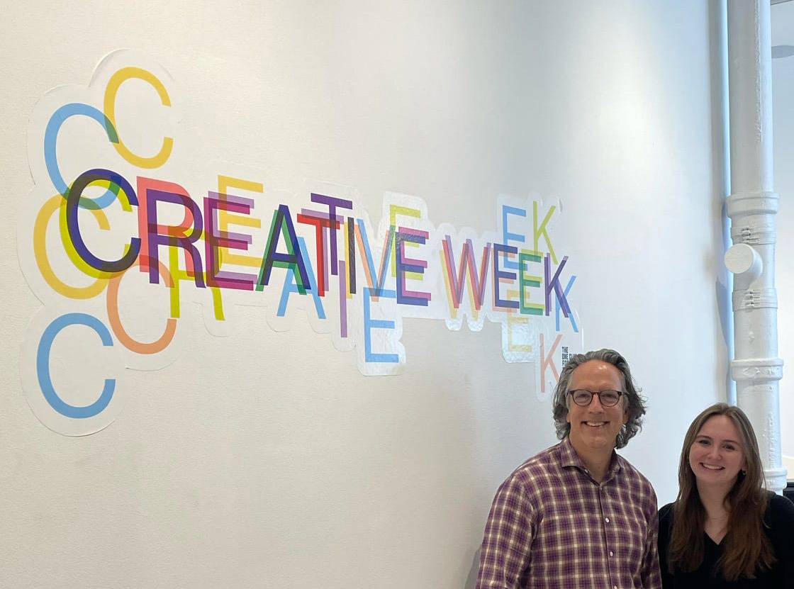 two individuals posing under a sign that says creative week