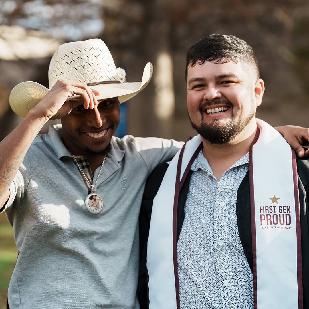 Two students in Sewell park after commencement with one wearing a first gen proud stole 