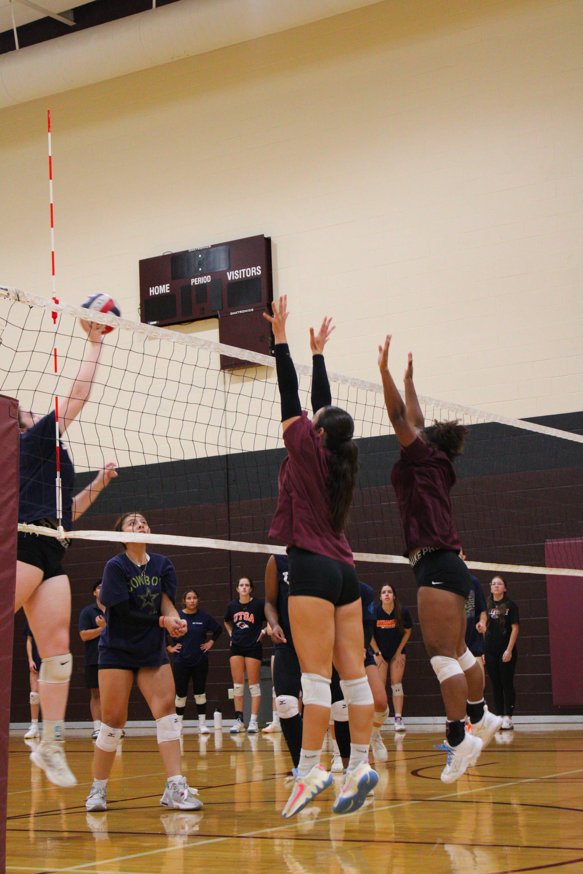 two women's volleyball club members blocking an opposing team spike