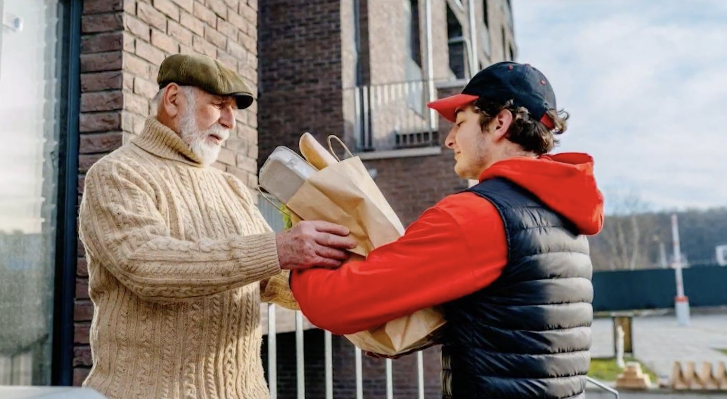 A young man giving an elderly man a bag full of groceries.