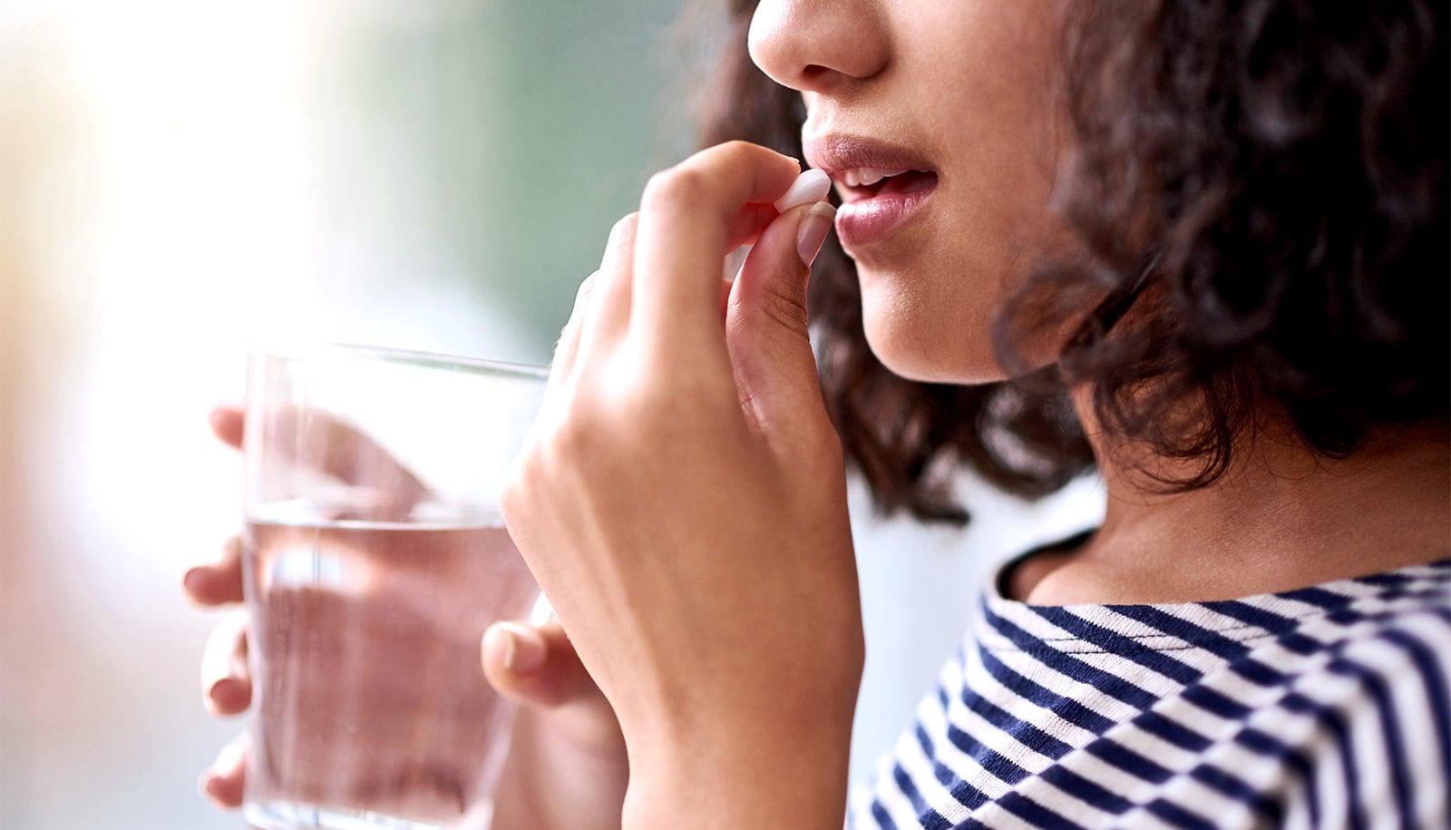 A lady holding water and a pill in her hands.