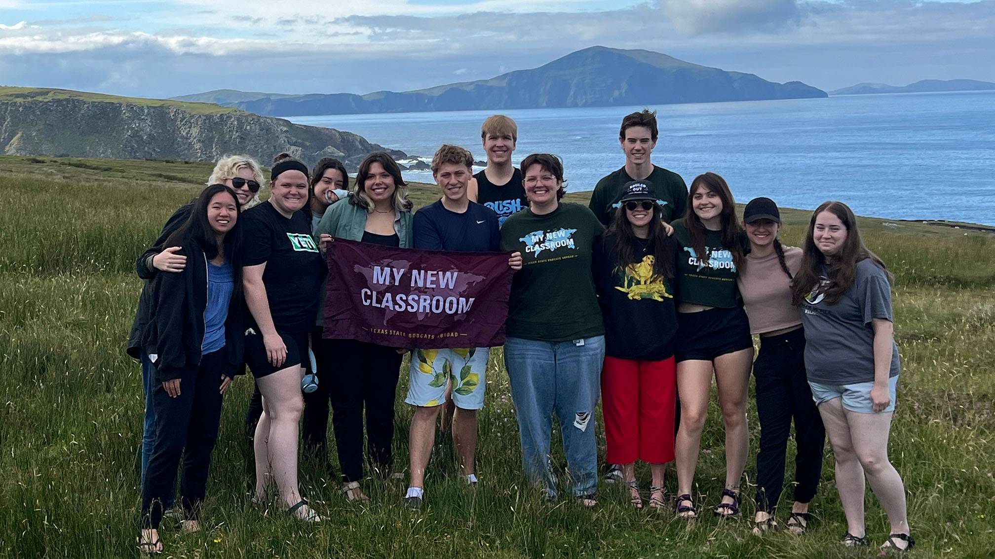 A group of students in a study abroad program pose for a photo in New Zealand with a TXST flag.