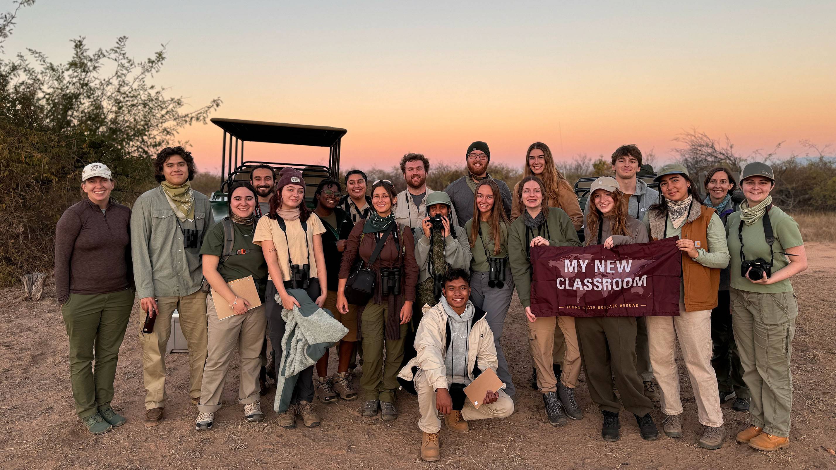 A group of students in a study abroad program pose for a photo together in Africa with a TXST flag.