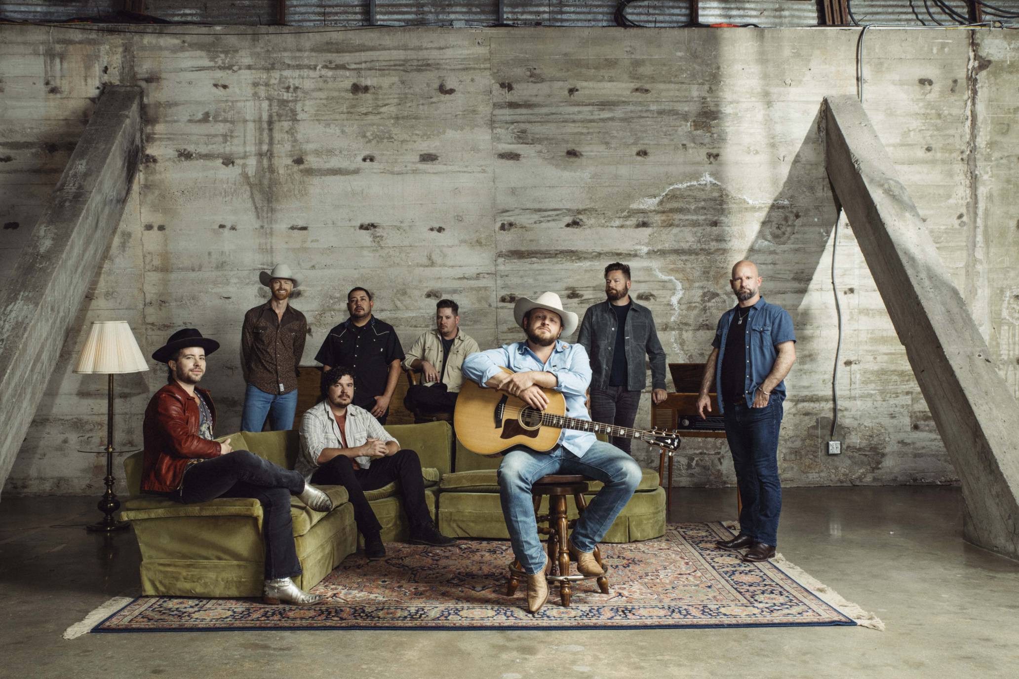 A group of people holding musical instruments and posing against an industrial backdrop