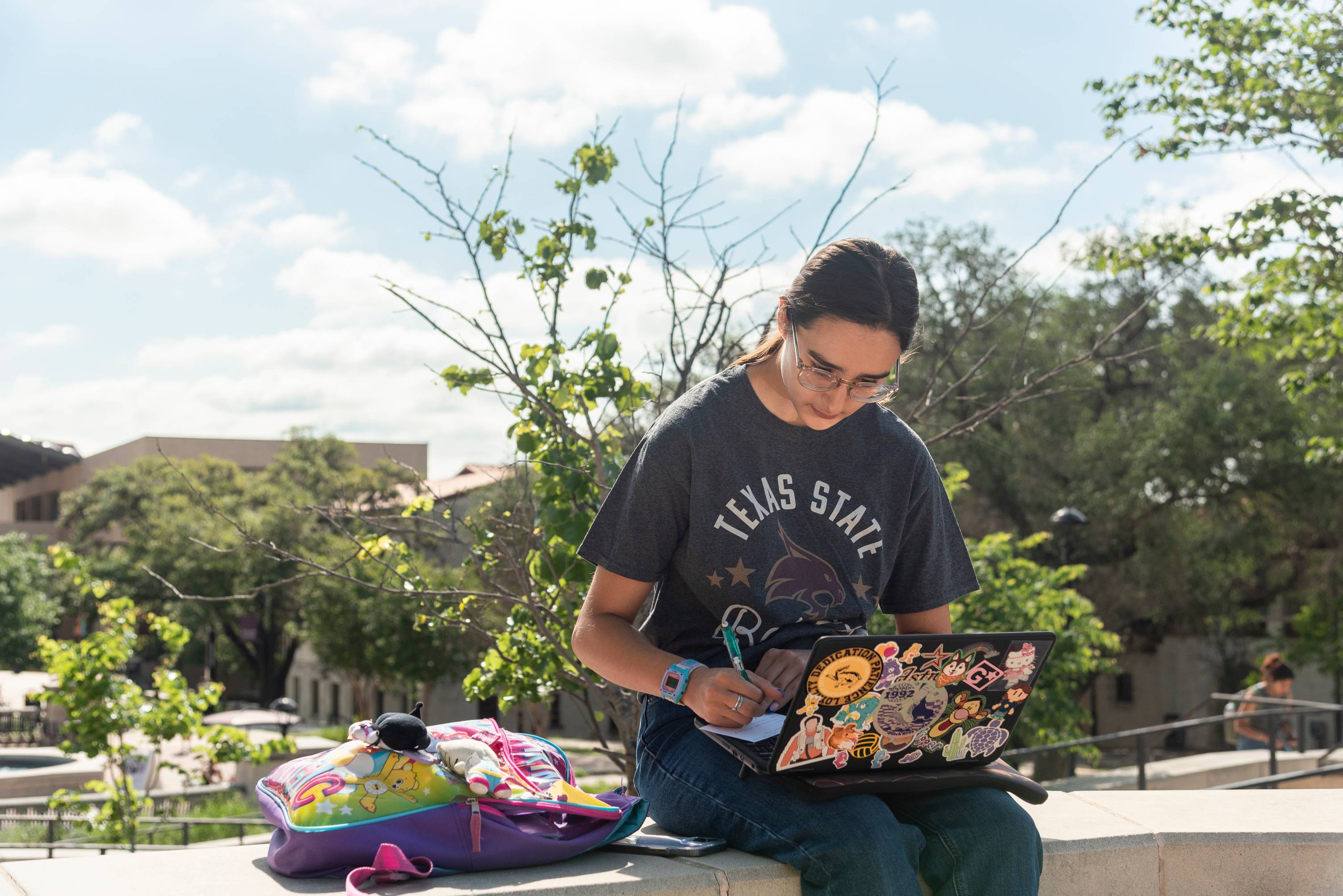 student sitting on ledge working on a laptop