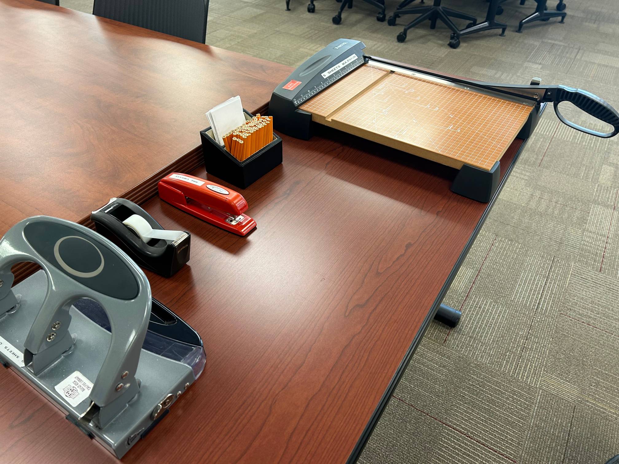 stapler, 3-hole punch, golf pencils, Scotch tape, and cutting board on a table