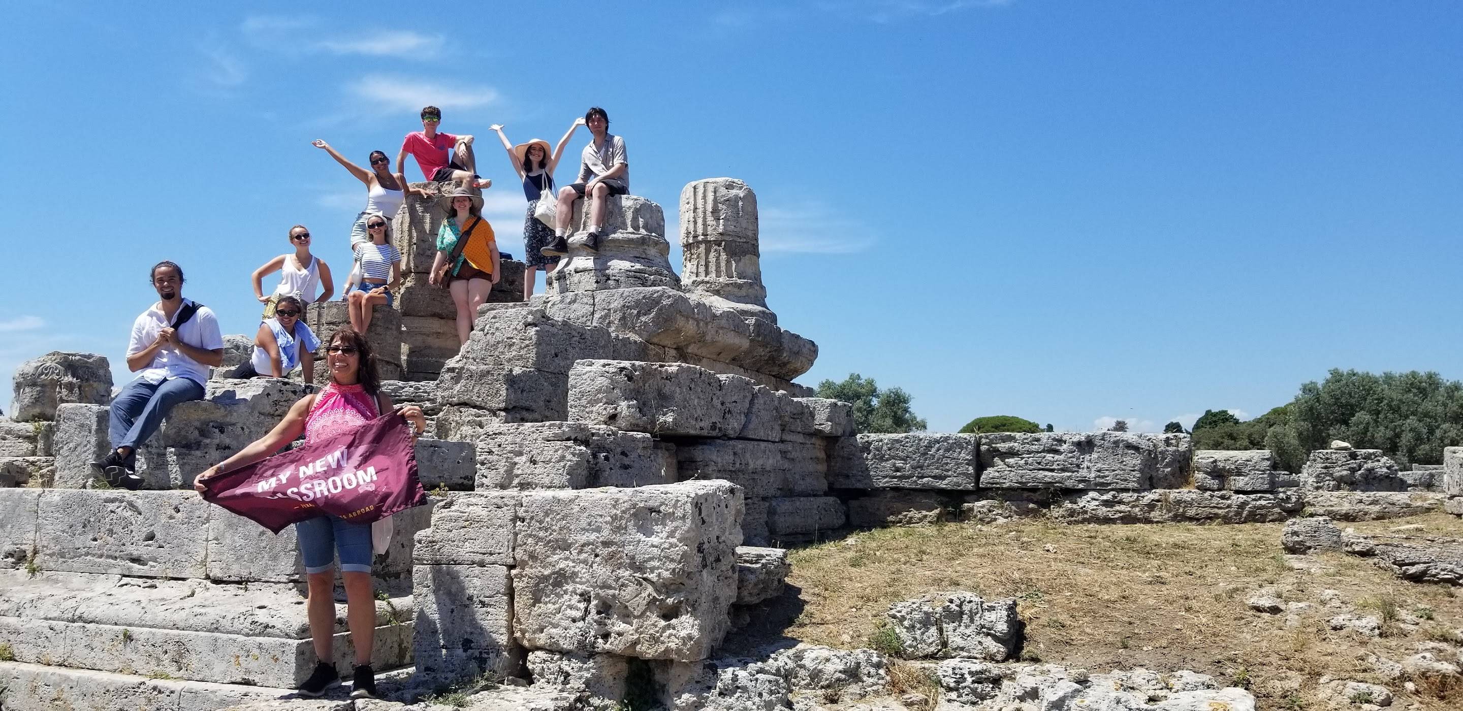 Group of students and one teacher on Paestum Forum, holding sign reading "My New Classroom"