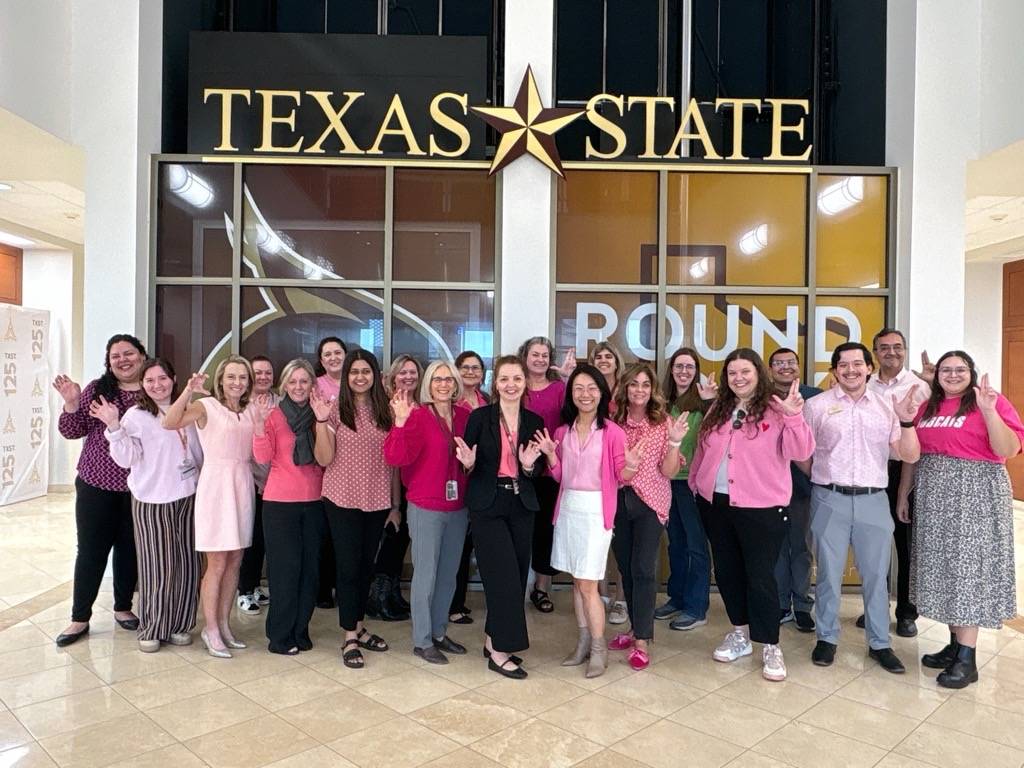 a group of txst employees posing in pink in avery at round rock campus