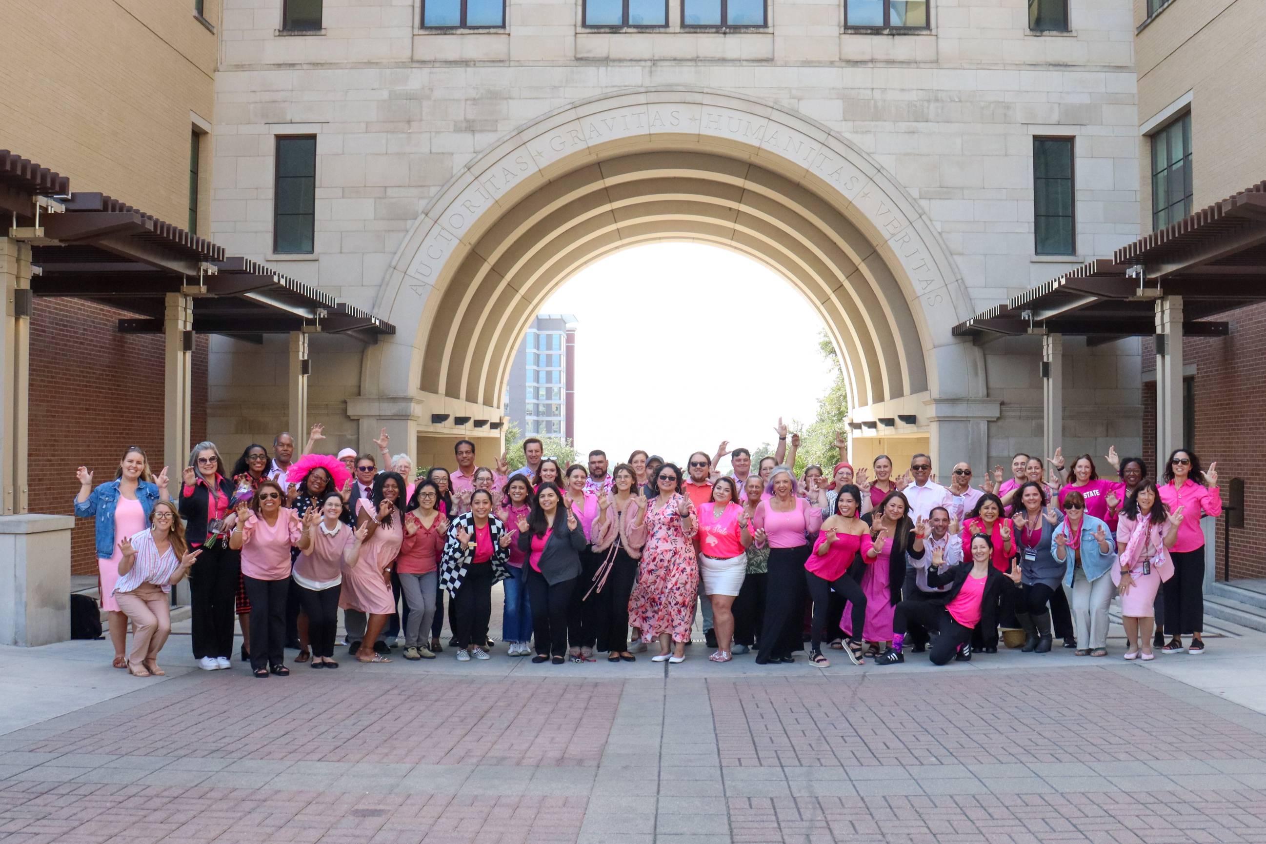 txst employees in pink gathered in front of the thh arch