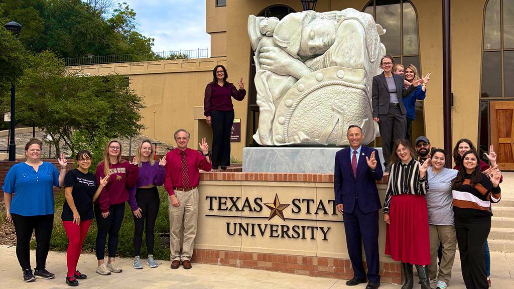 First Lady Beth and President Kelly Damphousse pose for a photo a group of Art and Design students and faculty member next to the Minerva statue.