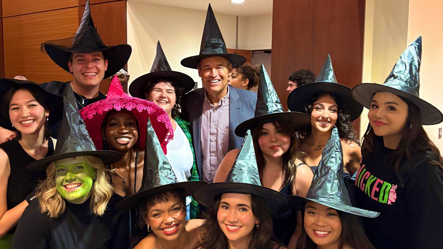 President Kelly Damphousse (back middle) poses for a photo with Musical Theatre students in witch hats.