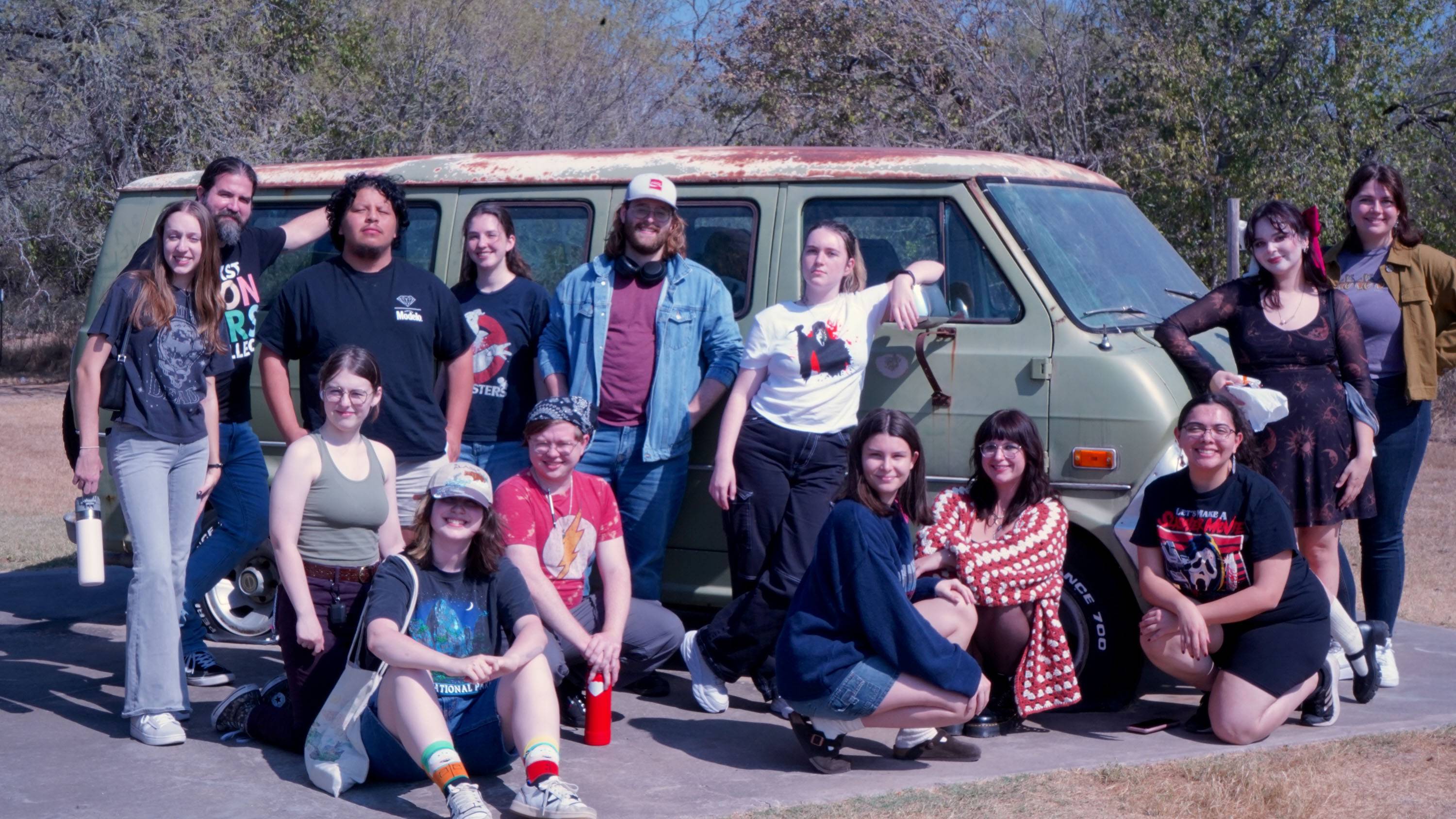 A group of students pose for a photo in front of a worn-down van at The Gas Station.