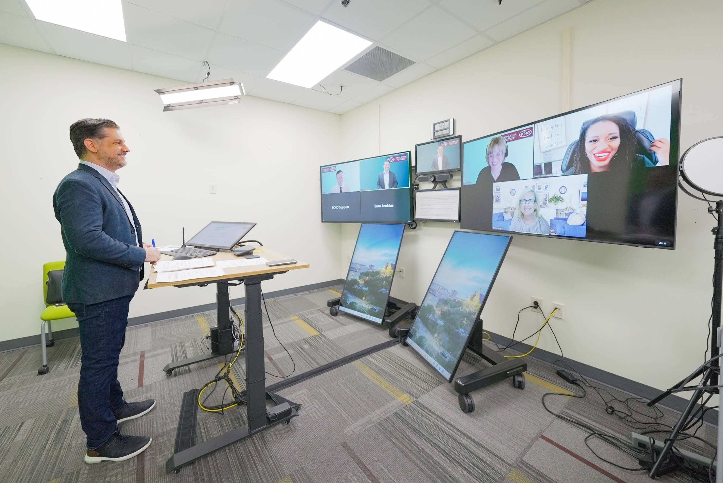 A photo of Dr. Josh Daspit hosting a virtual learning network in front of four TV screens.