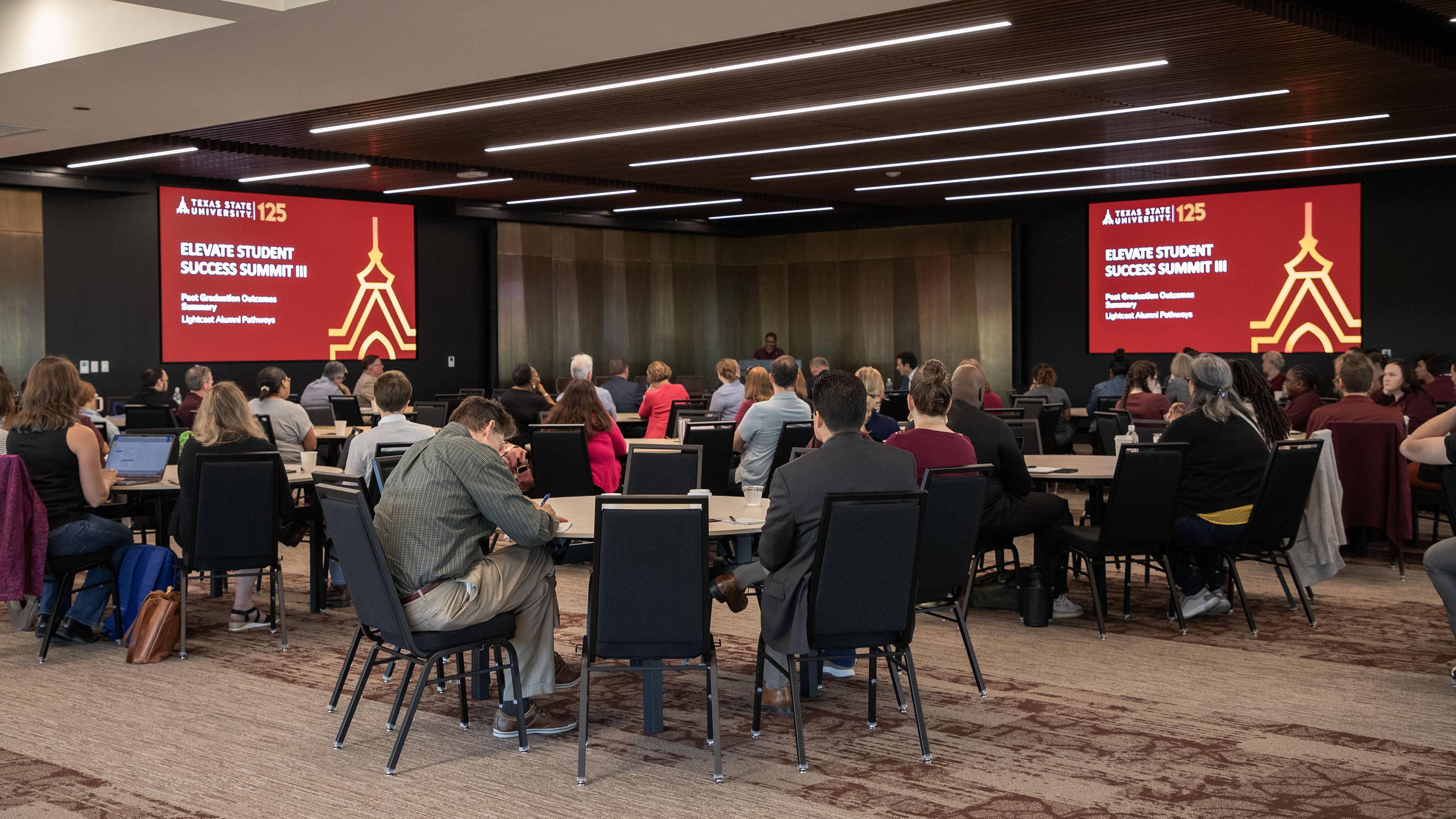 Several tables of people take notes and listen to speakers at the Elevate Employability Summit.