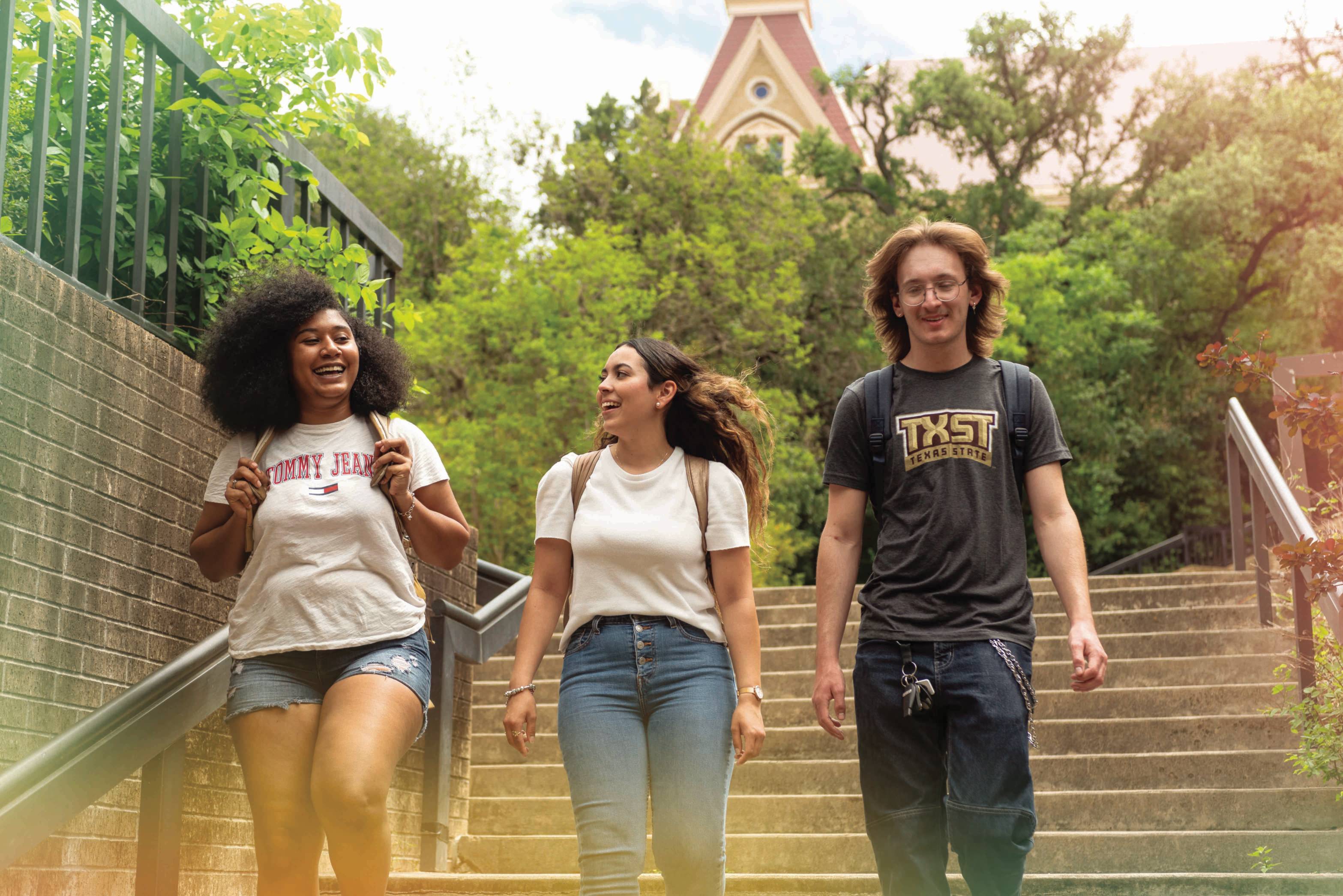 Three young folks wearing backpacks laugh and talk while they descend a flight of stairs.