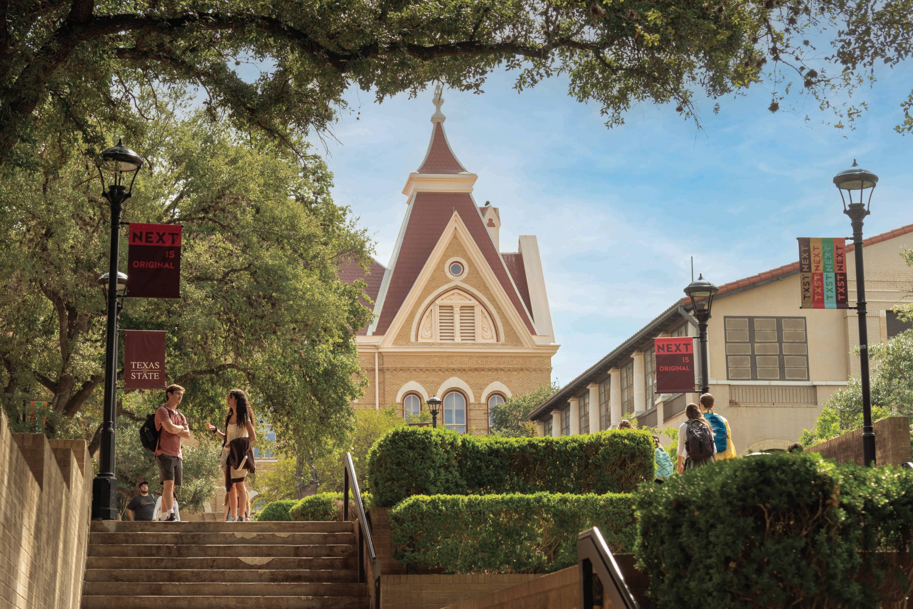 Artful shot of the San Marcos campus, showcasing a stairway, greenery, and the Old Main building in the background.