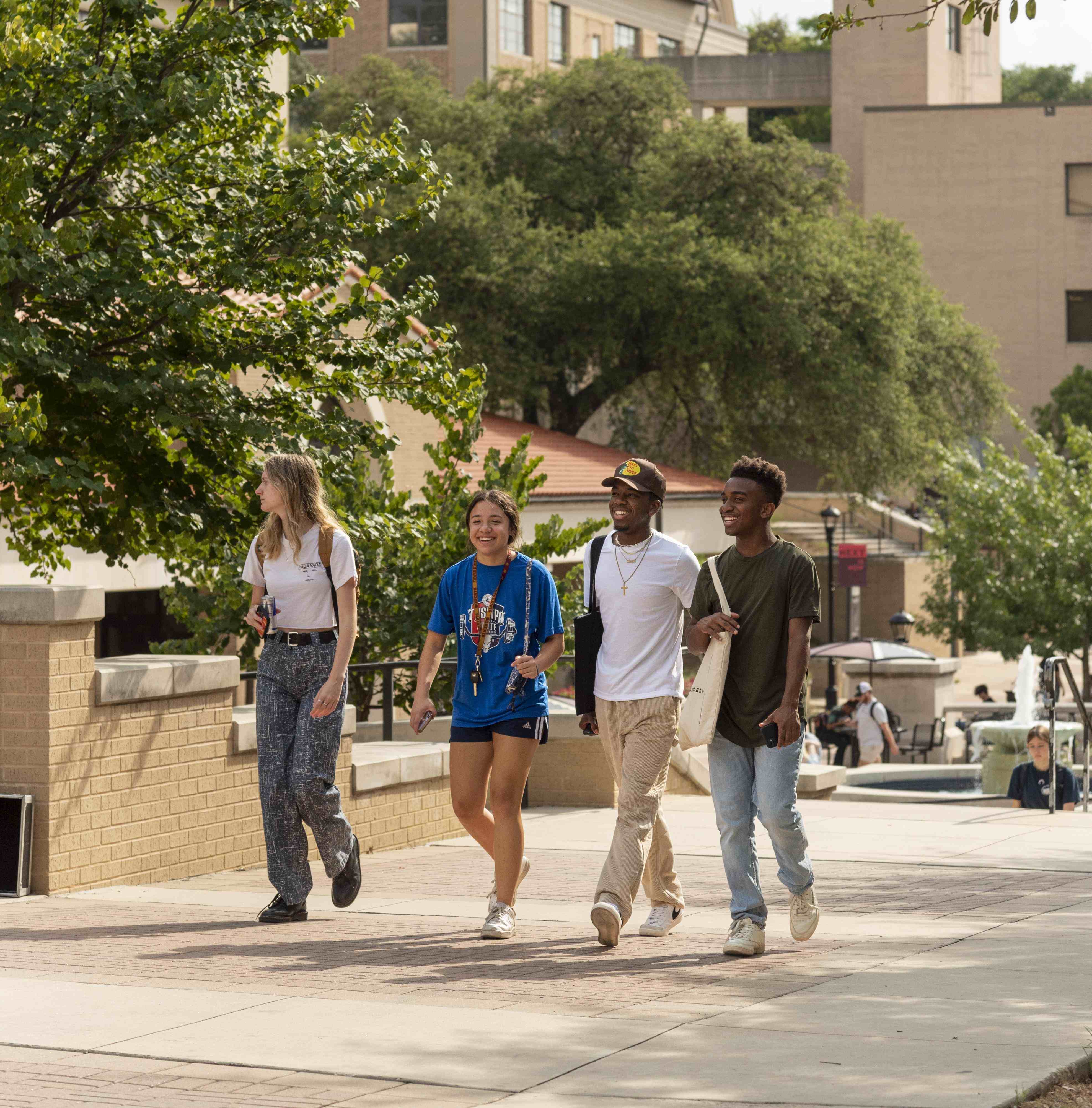 Four students talk and laugh while walking through campus.