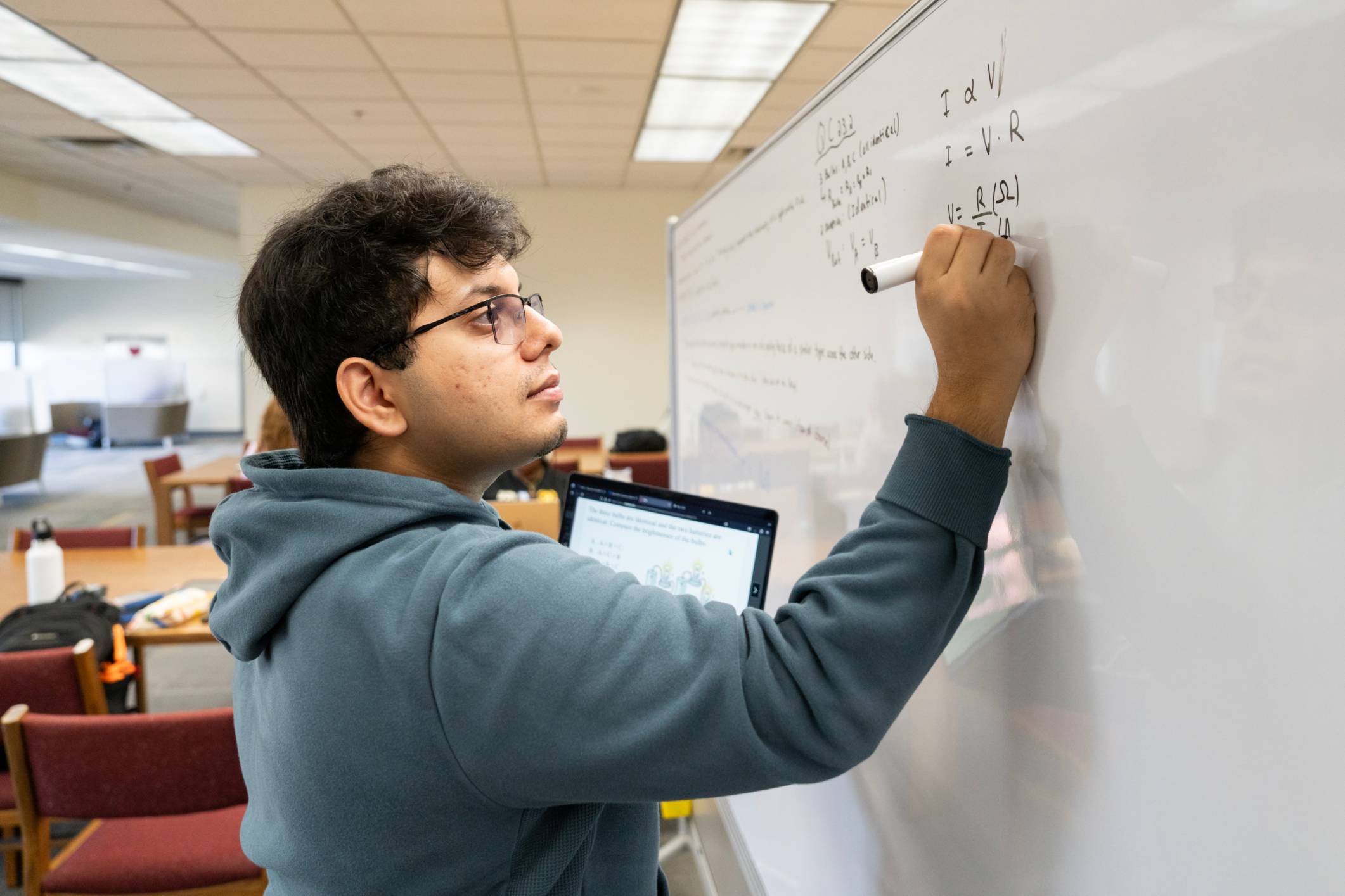 A standing student writes on a whiteboard.