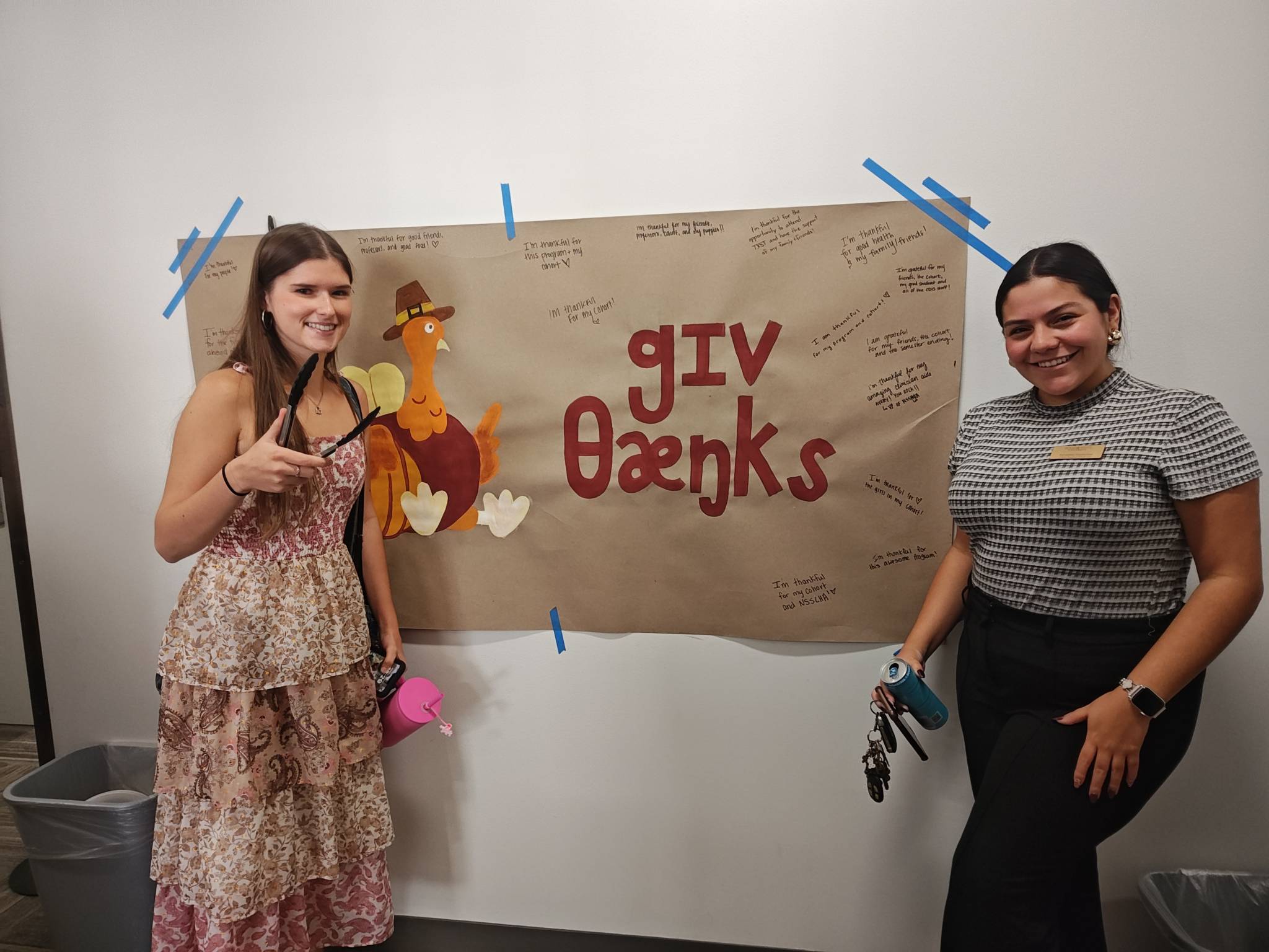 Two CDIS students standing next to the "Give Thanks" poster.