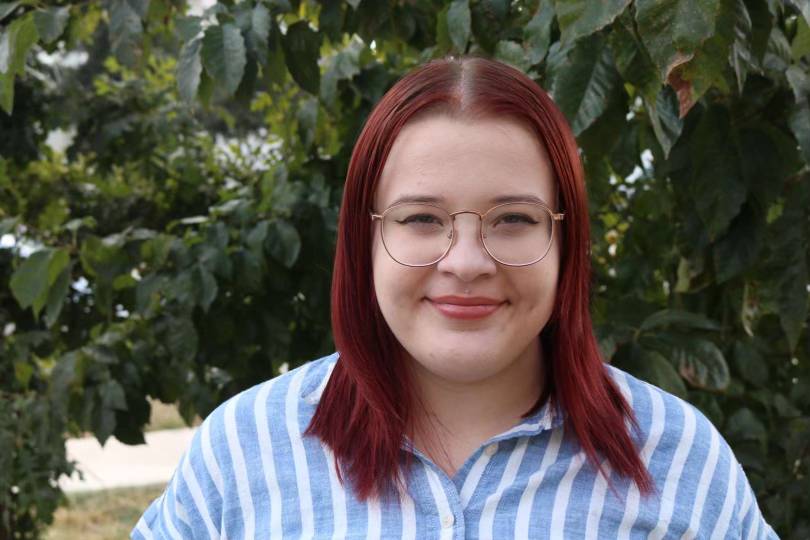 woman with red hair and glasses in front of trees