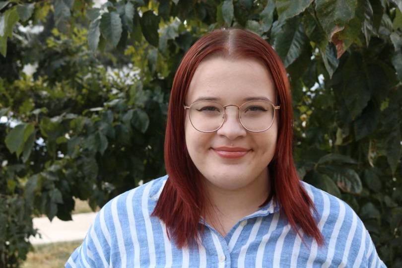 woman with red hair, glasses, trees behind her