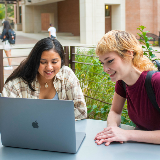 Two students smiling while working on a laptop