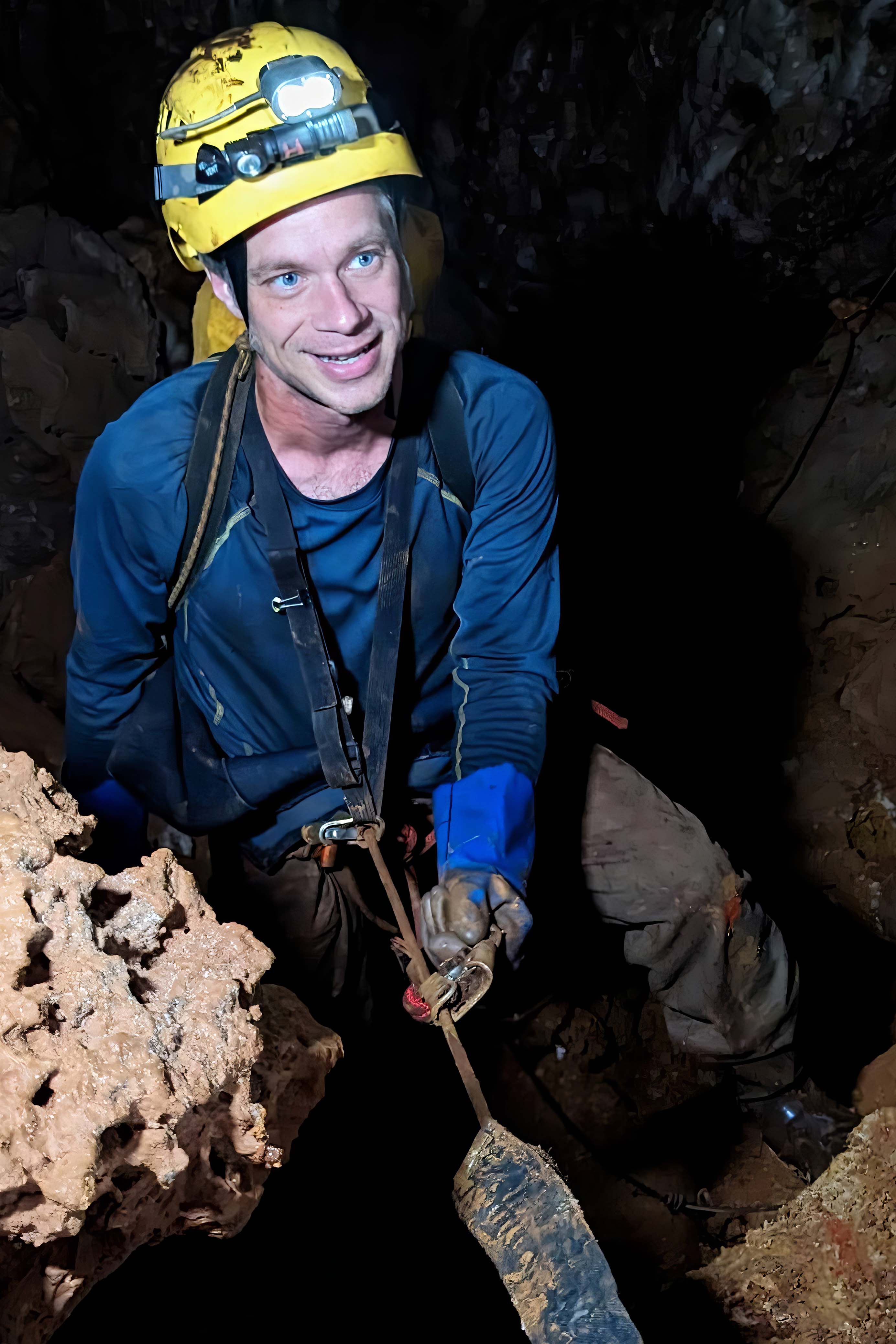 Ben Hutchins ropes down into a cave wearing a hardhat.