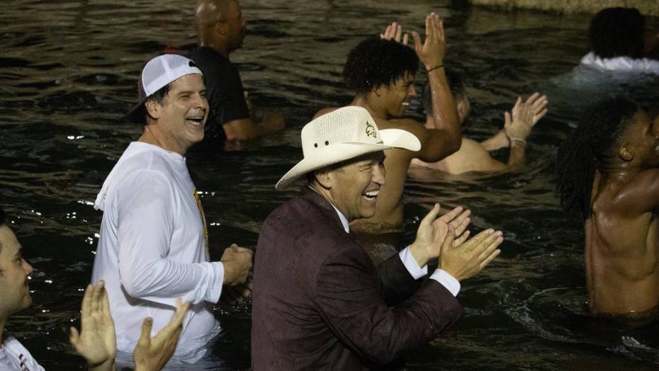 Don Coryell (left) and President Kelly Damphousse celebrate in the river with football players.