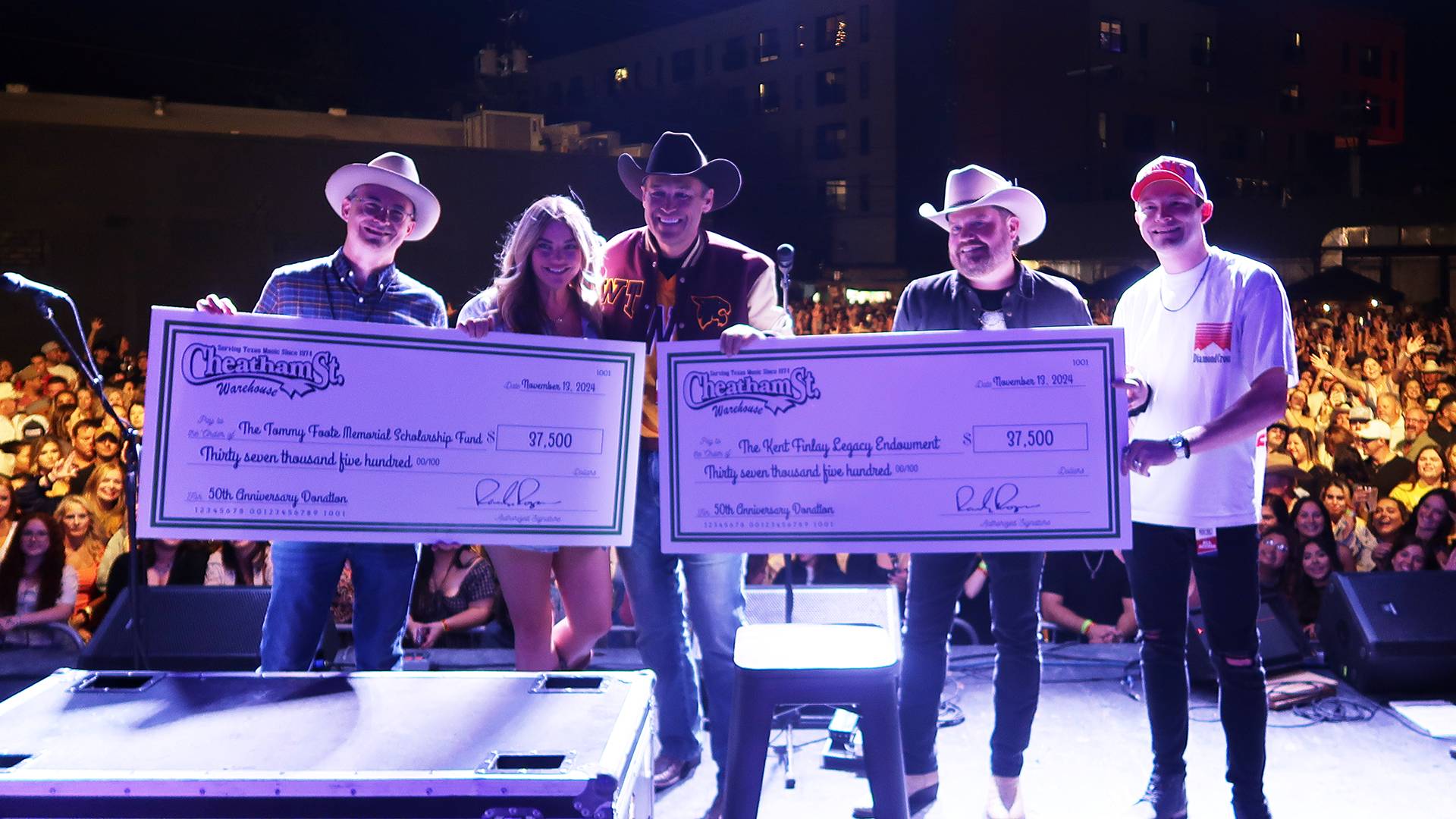 Randy Rodgers, Texas State President Damphousse, and friends holding up two checks on stage at Cheatham Street Warehouse for the Kent Finlay Legacy Endowed Scholarship and the Tommy Foote Memorial Scholarship