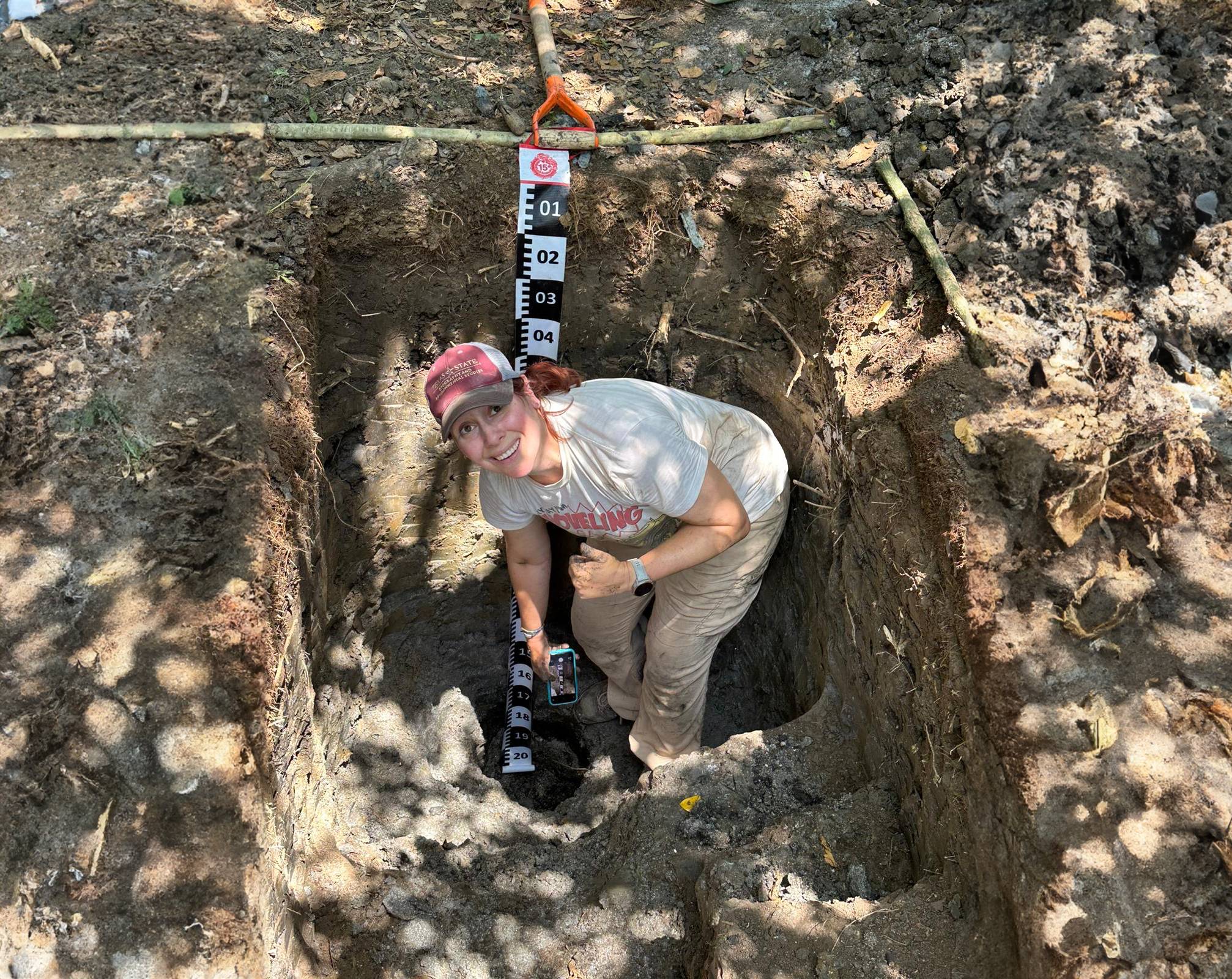 a researcher in a hole surveying artifacts 