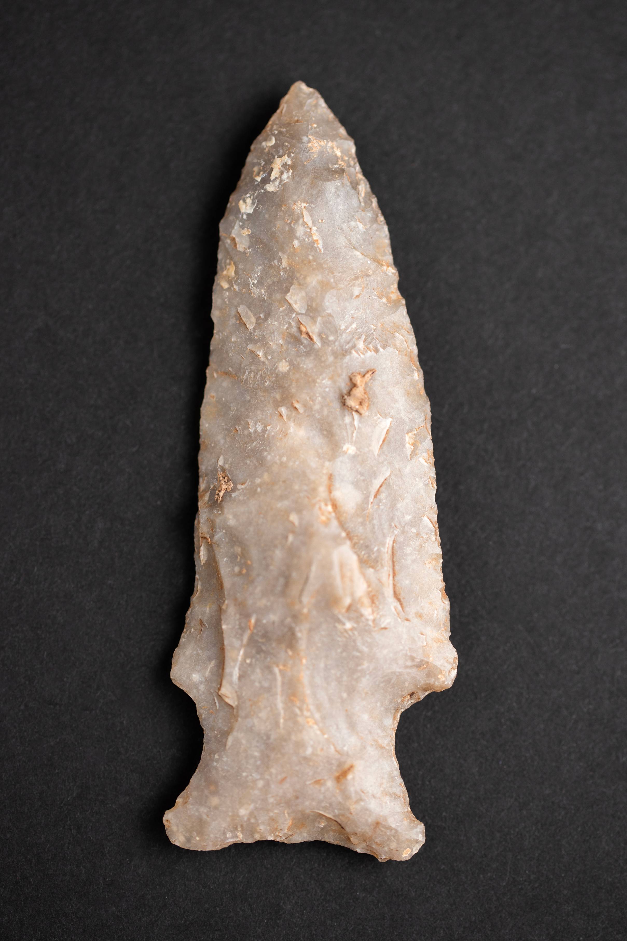 Projectile point made out of pale stone on black background.