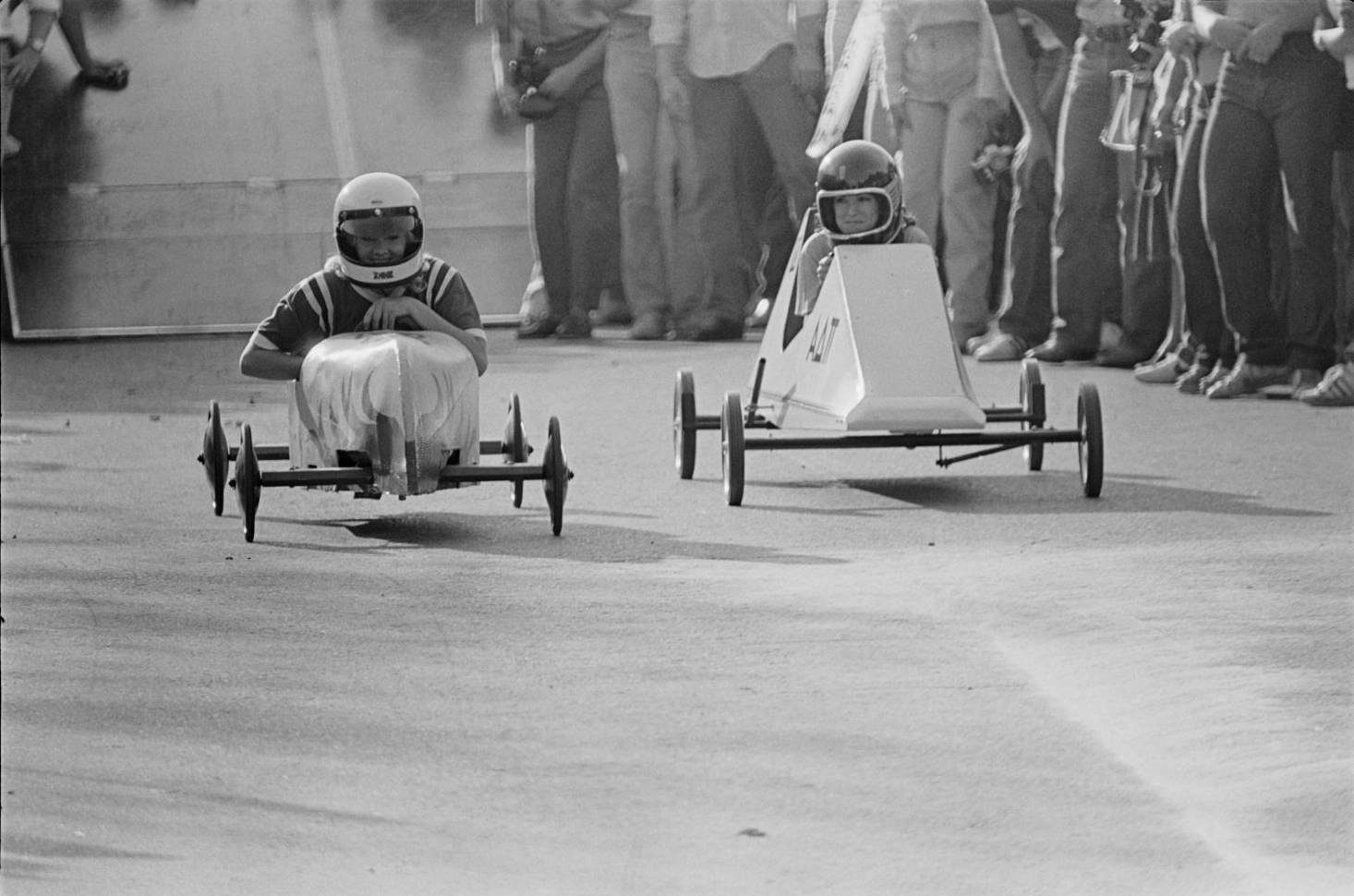 Vintage yearbook photo of two students racing in simple soapbox derby cars. 