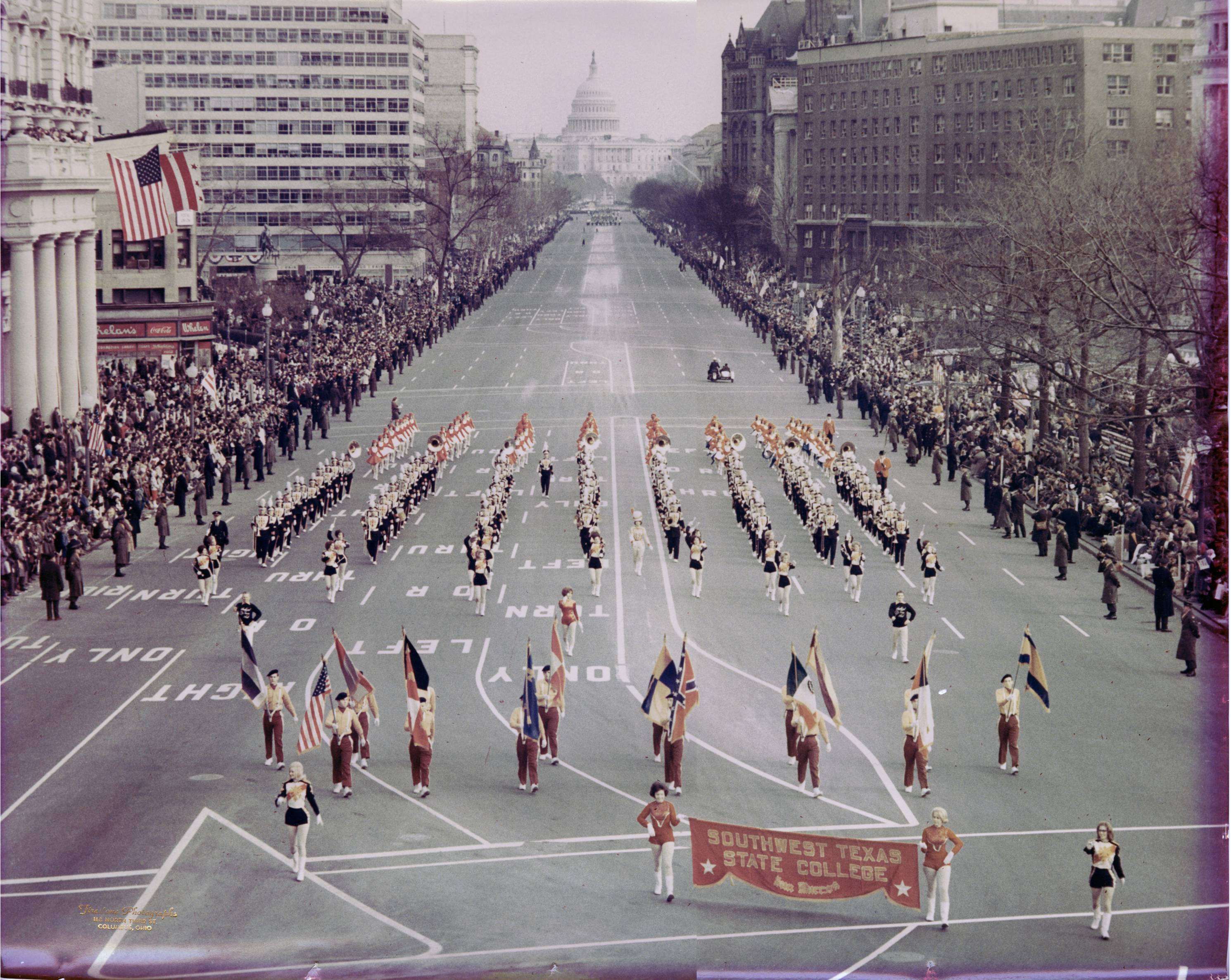 The Bobcat marching band performing in a parade in Washington D.C, marching down East Capitol Street. The dome of the U.S. Capitol building can be seen in the distance.