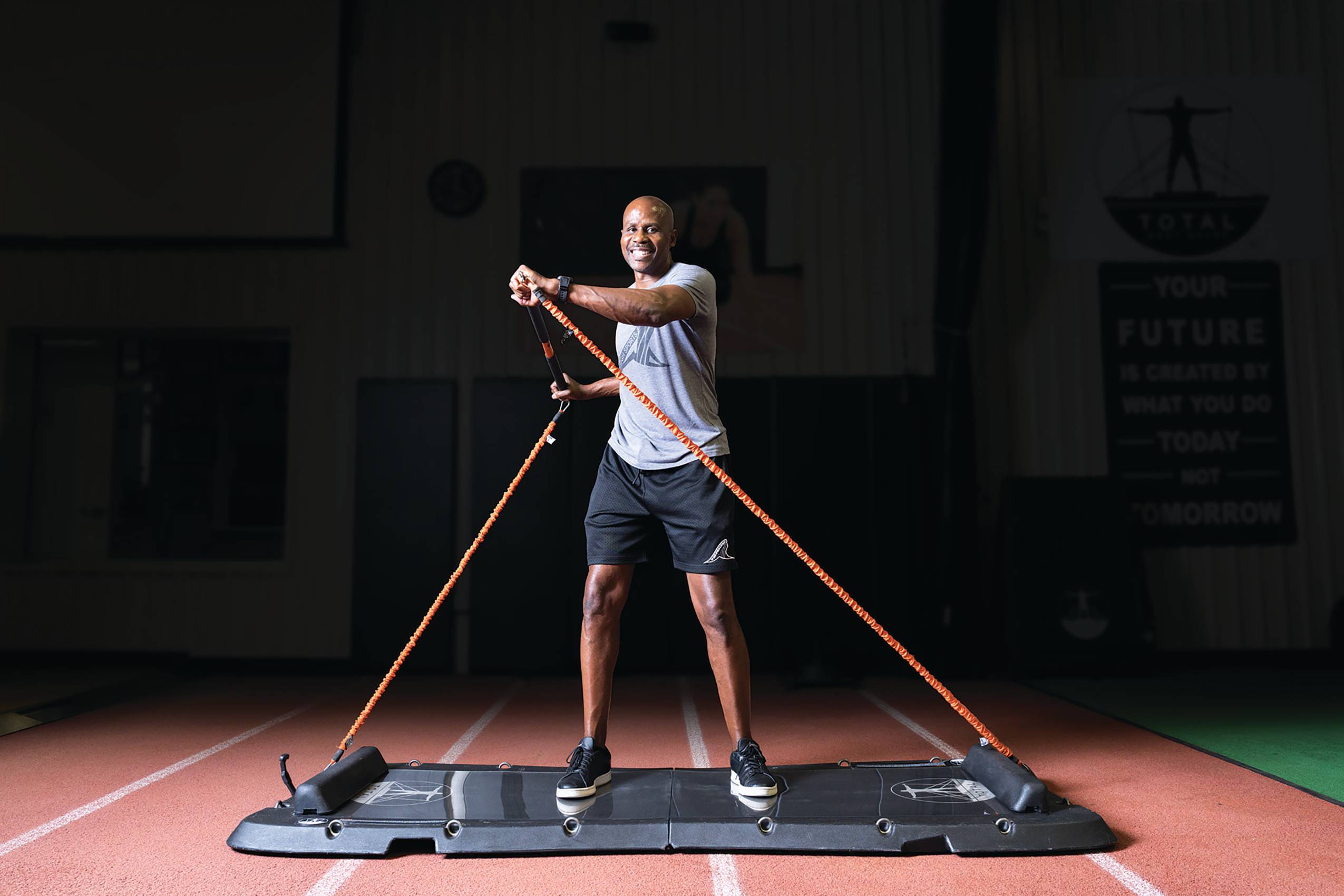 Charles Austin demonstrating his Total Body Board, a piece of gym equipment that uses resistance bands for a variety of exercises.