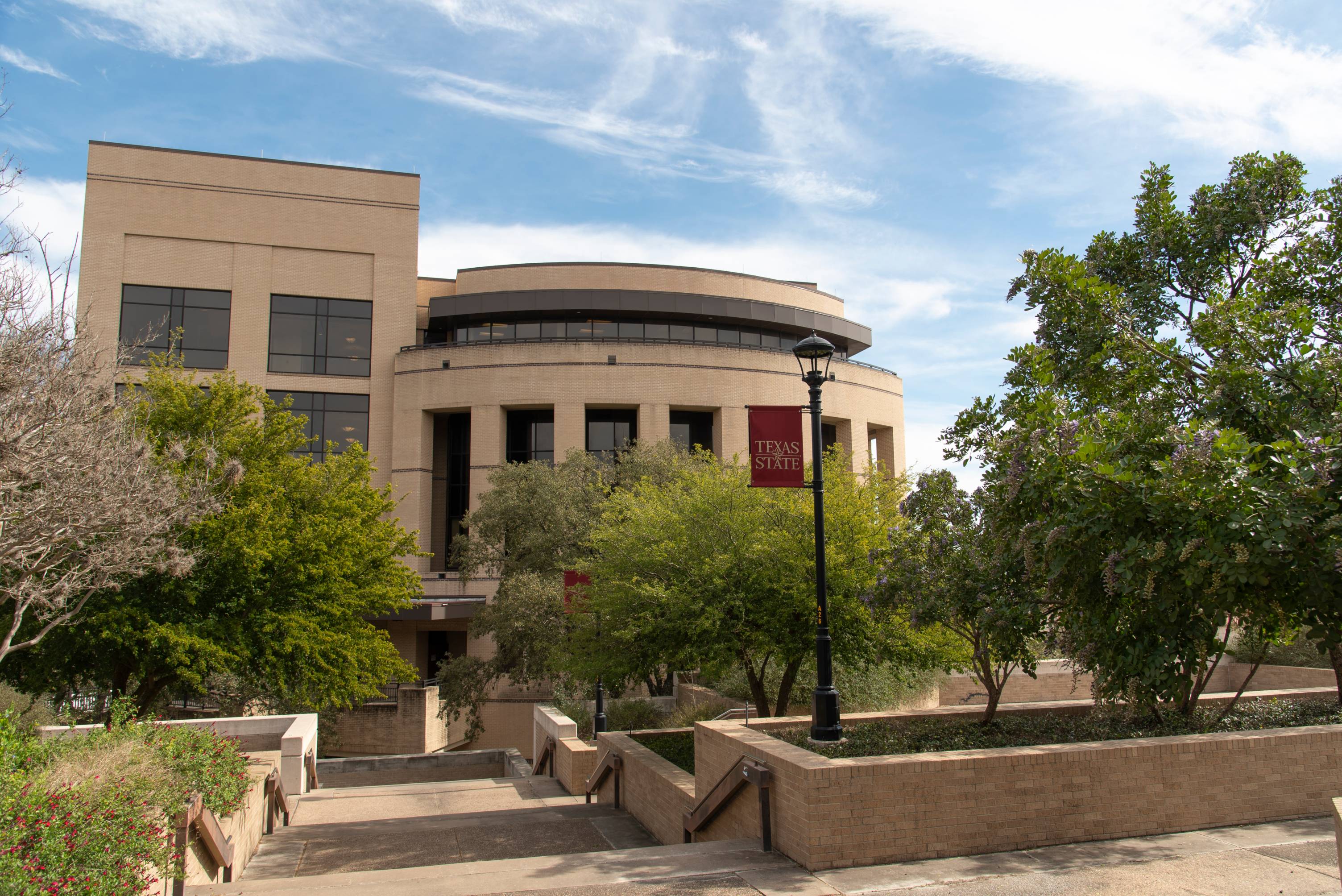 Texas State University's McCoy College of Business with trees and a light post in the foreground.