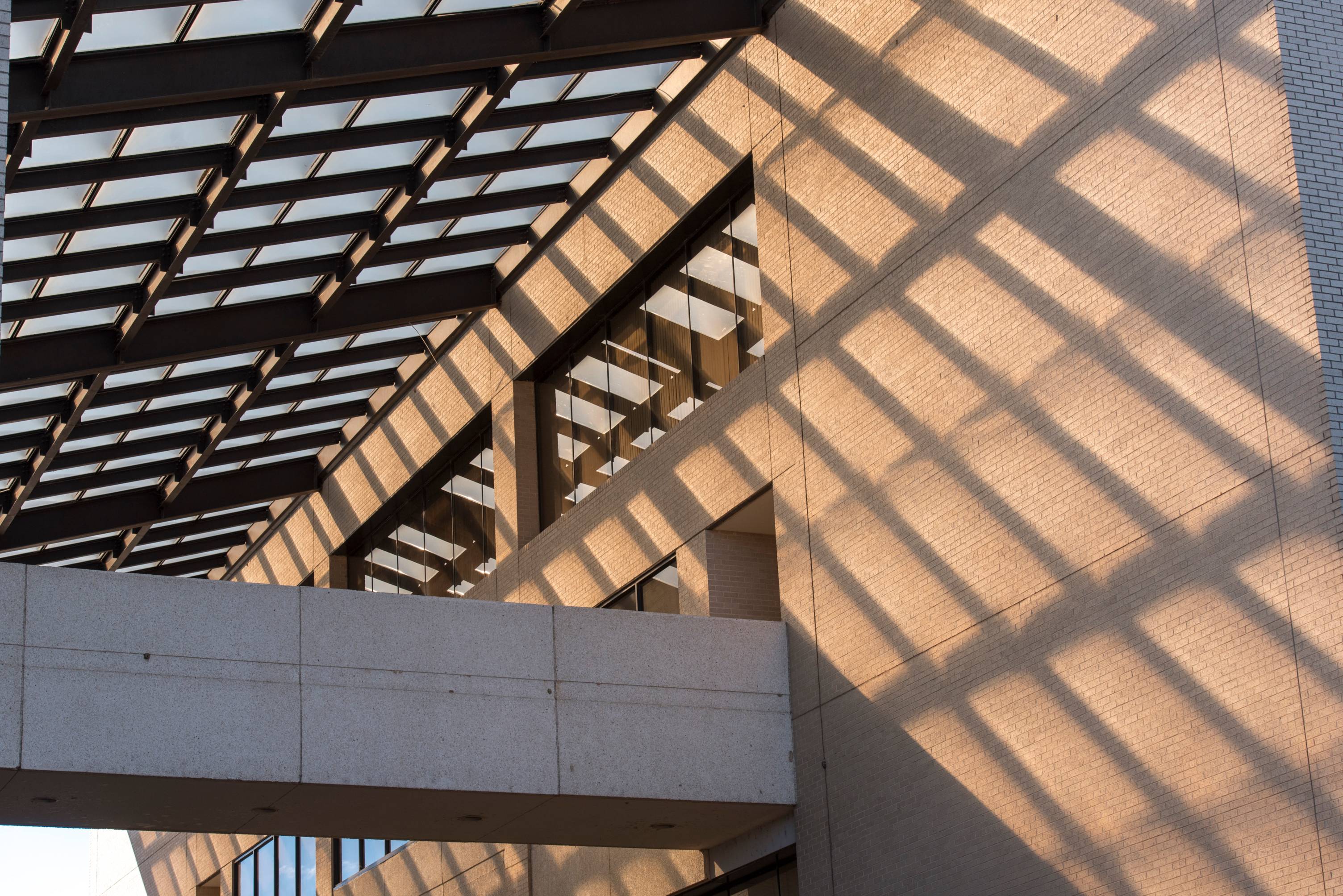 The glass-paneled roof of The Den cascades shadows onto the side of the building.