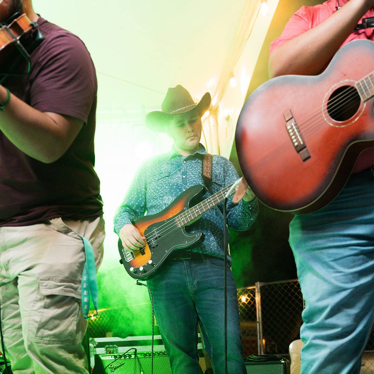 The Bobcat Band performs, a young man in a cowboy hat plays a bass guitar, partially obscured behind several other band members.