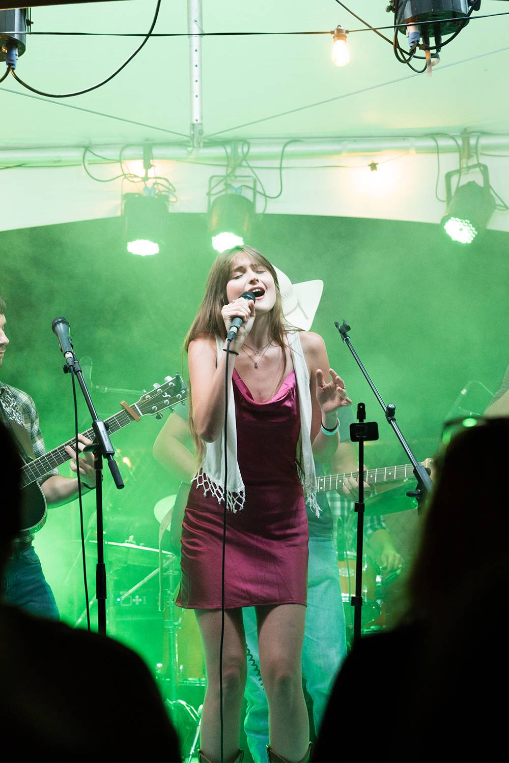 AnaBelle Elliot performing with Bobcat Country. AnaBelle is singing lead for this song, the whole band is partially obscured with fog and green lighting effects.