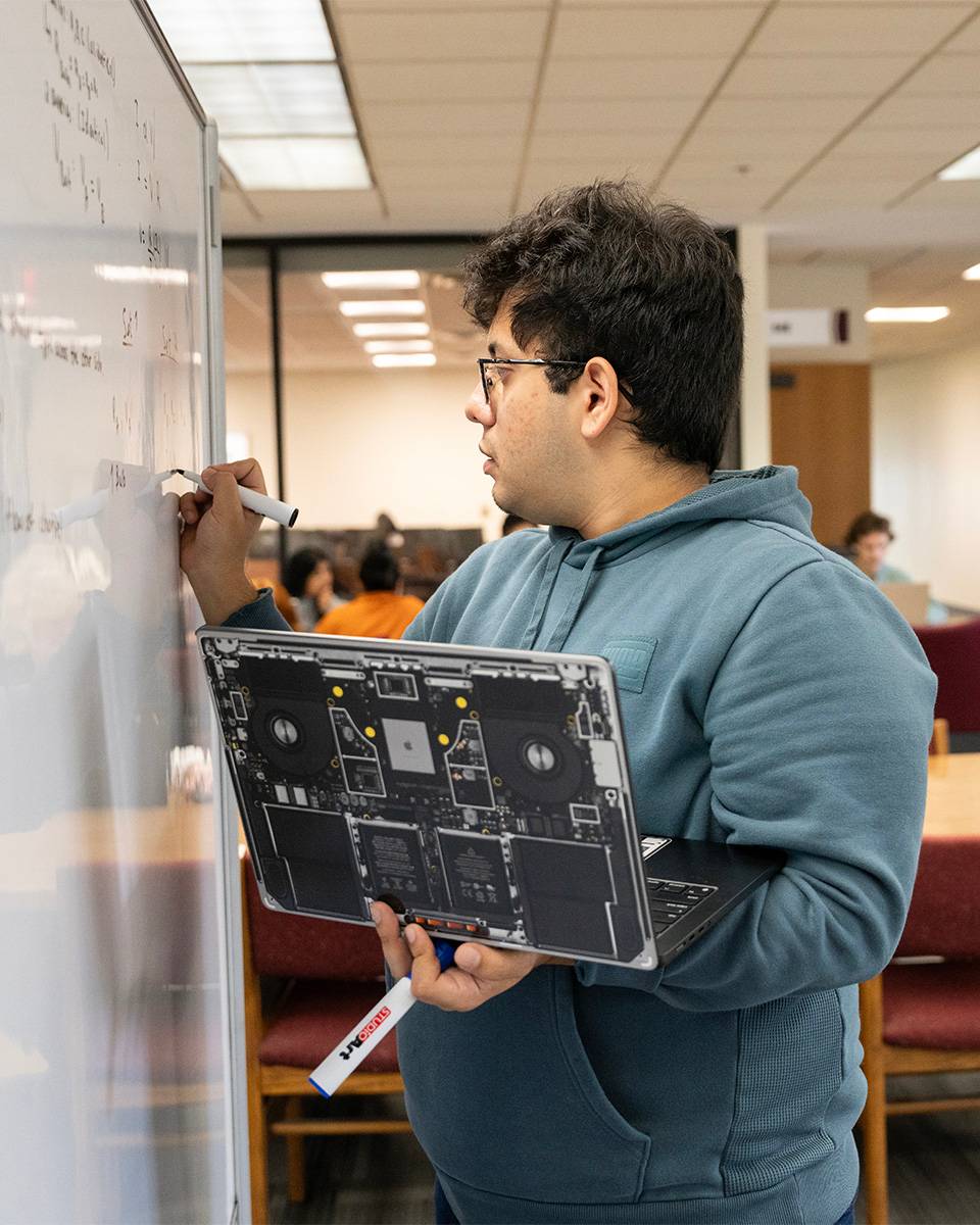 A student working out math formulas on a white board at Alkek Library.