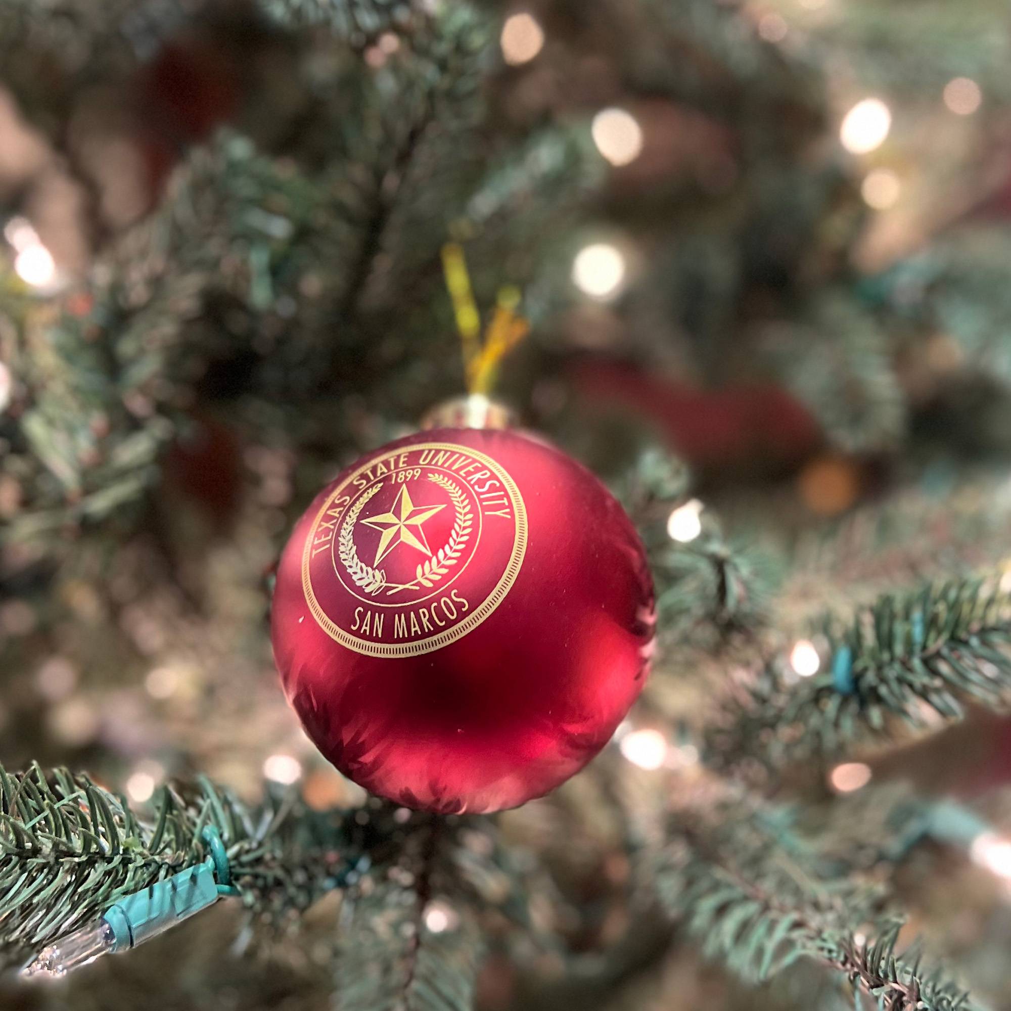 Maroon holiday ornament ball featuring gold Texas State University seal