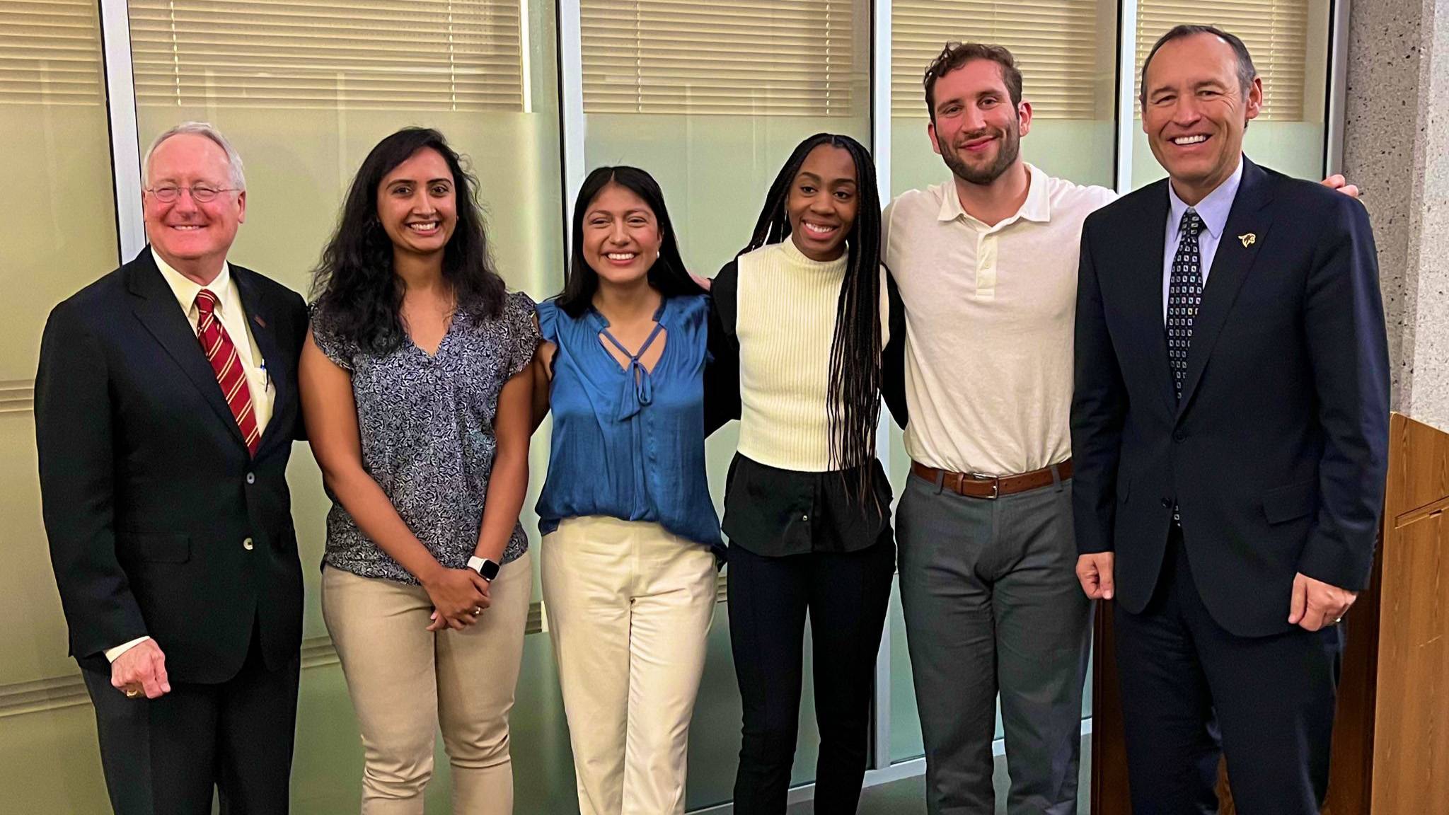 A group of students pose for a photo with Brian McCoy (left) and President Kelly Damphousse (right).