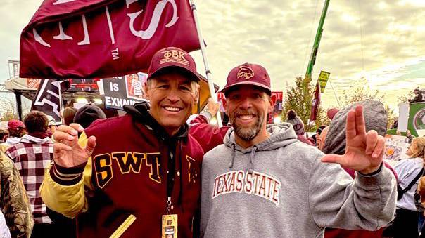 President Kelly Damphousse (left) poses for a photo with a TXST alum with the TXST flag flying behind them.