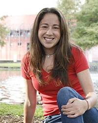 Ashley “Annie” A. Lozano sits in front of a pond with one knee up.