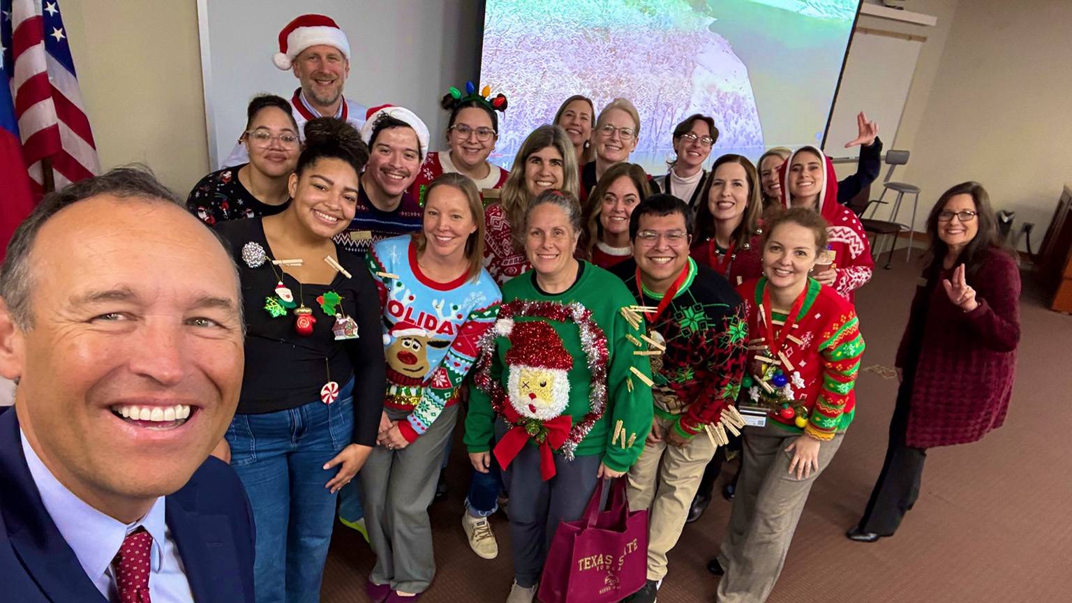 President Kelly Damphousse (left) takes a selfie with a group of students in holiday outfits.